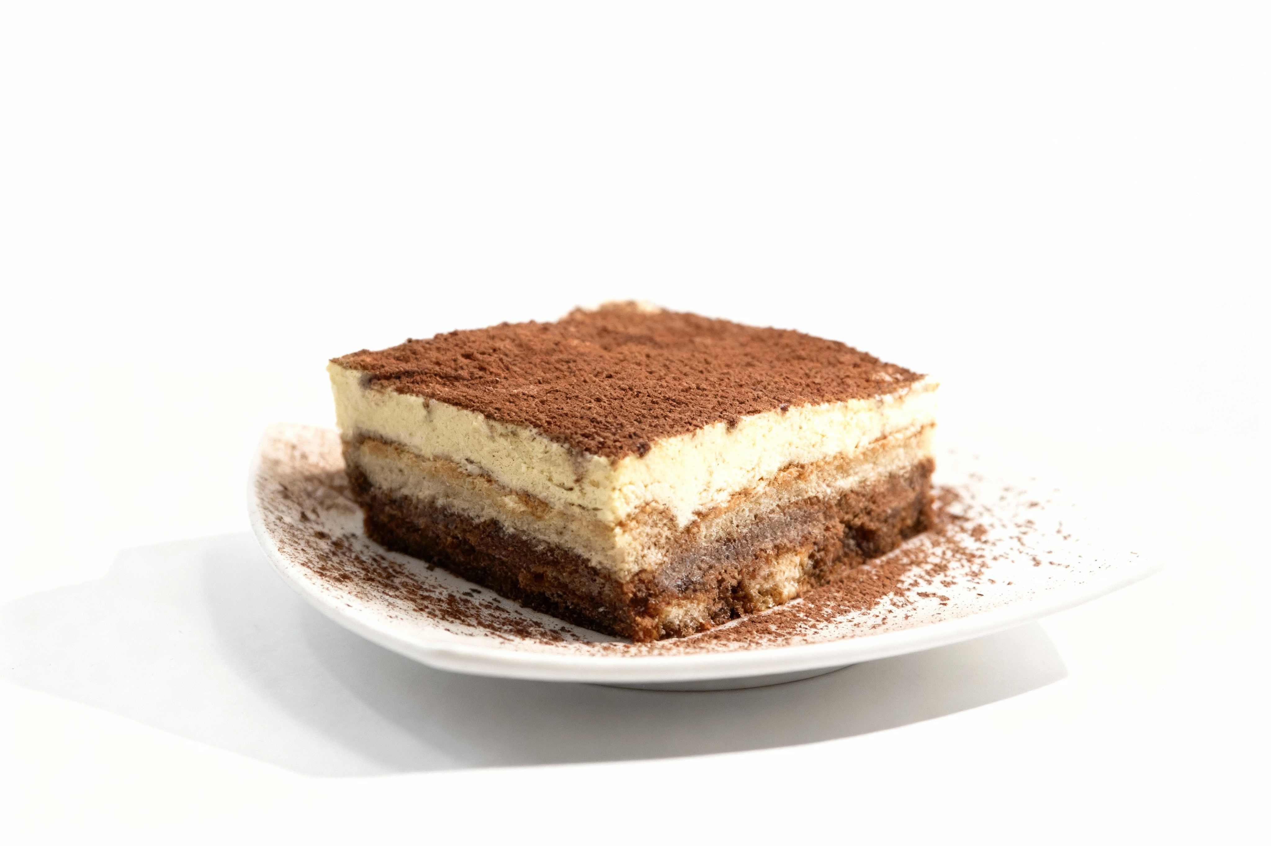 Square slice of tiramisu featuring layers of coffee-soaked ladyfingers and mascarpone cream topped with a thick dusting of cocoa powder.