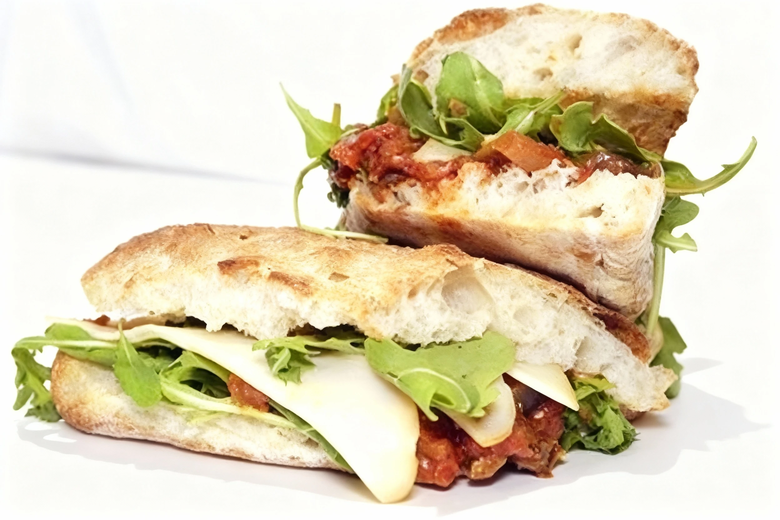 A ciabatta sandwich cut in half, filled with sliced provolone cheese, fresh arugula, and sun-dried tomatoes or red pepper spread.
