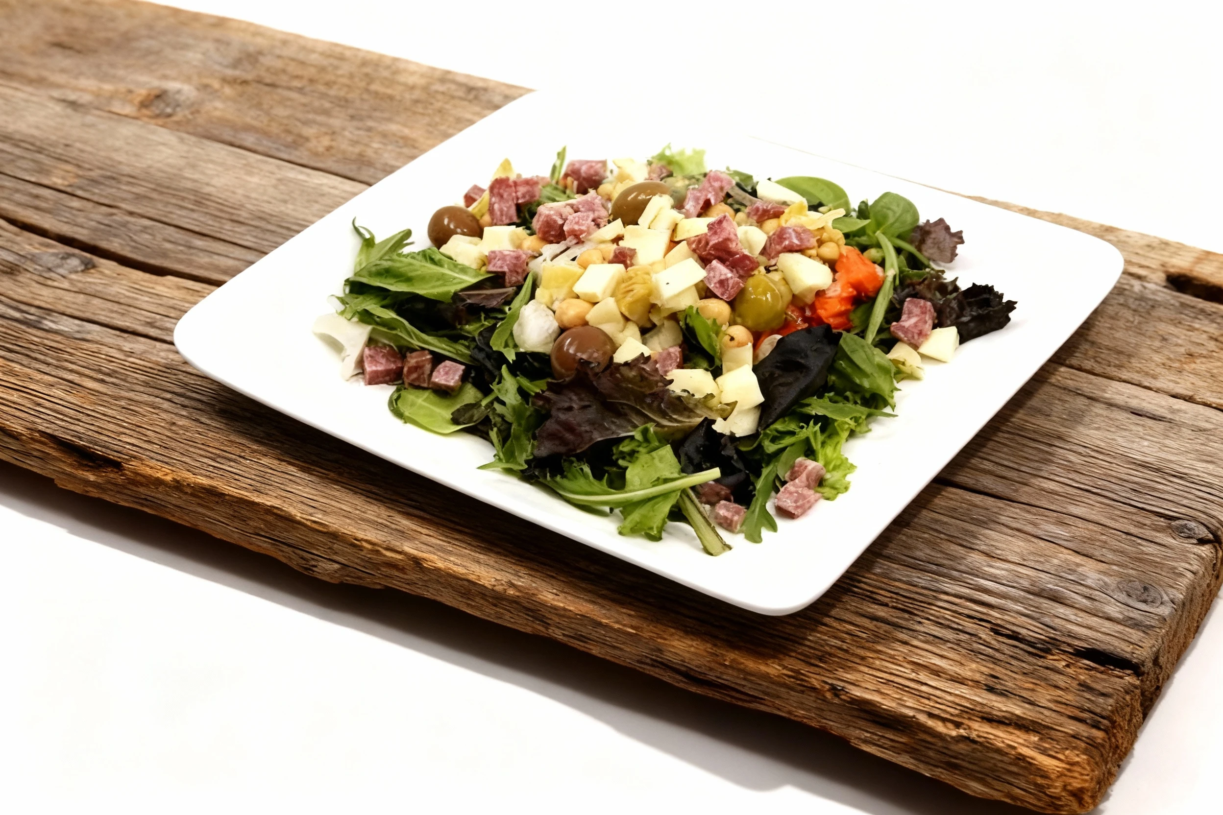 Antipasto salad featuring mixed greens topped with cubed salami, diced cheese, whole olives, and chickpeas on a white rectangular plate.