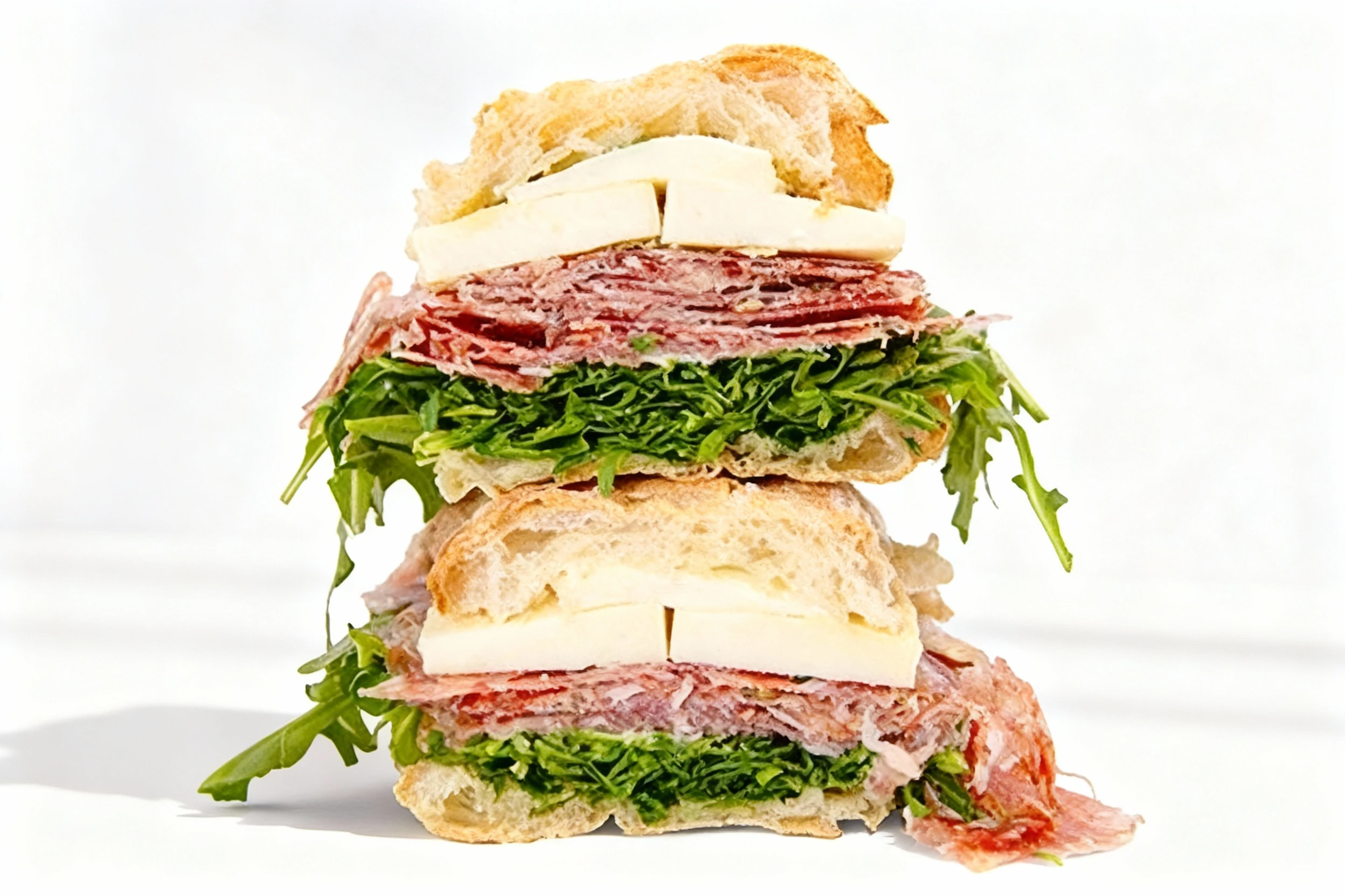 A stacked ciabatta sandwich filled with thick slices of mozzarella cheese, layers of cured salami, and a generous bed of fresh arugula.
