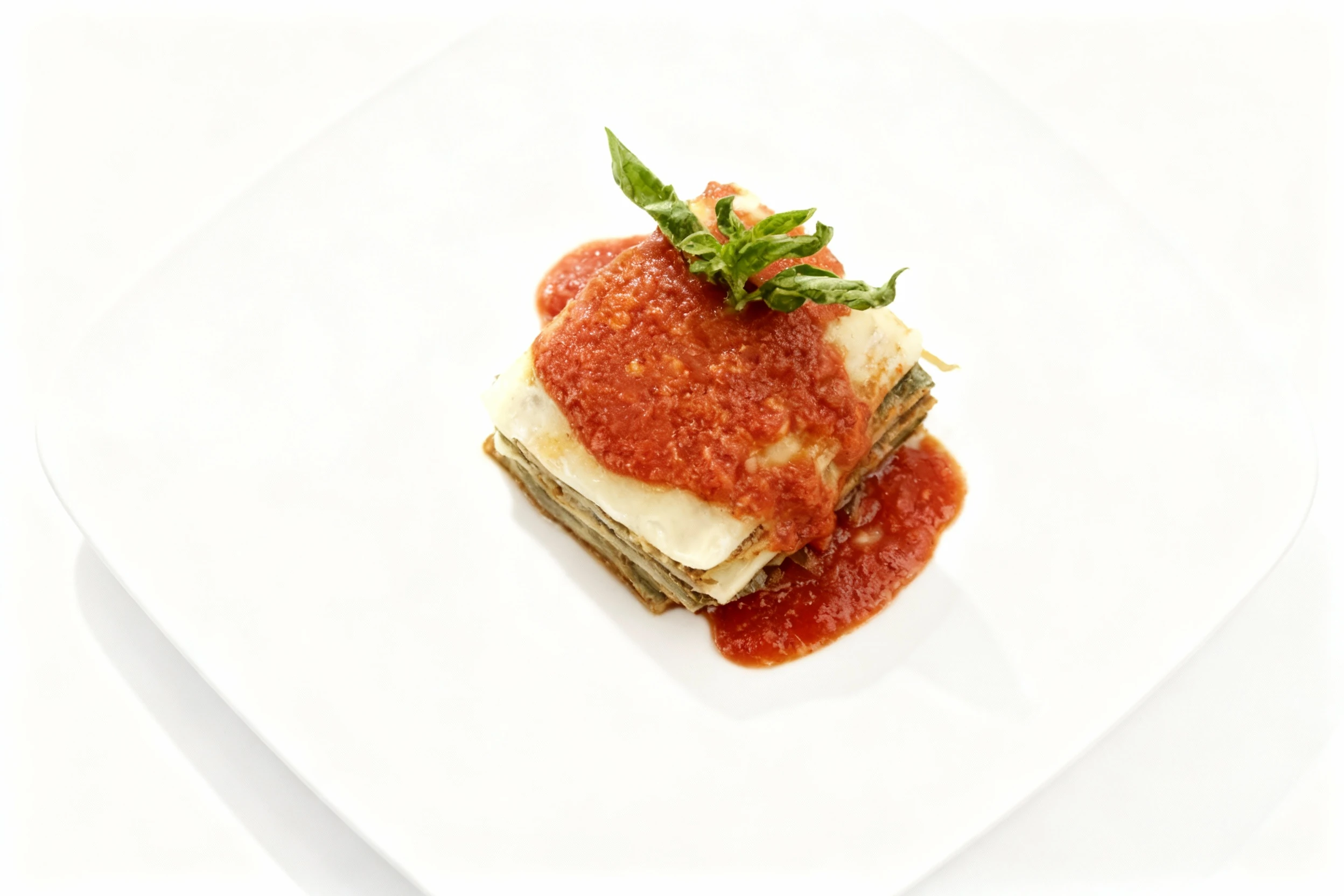 Square-cut vegetable lasagna layered with white sauce and topped with thick tomato marinara and a fresh basil garnish.