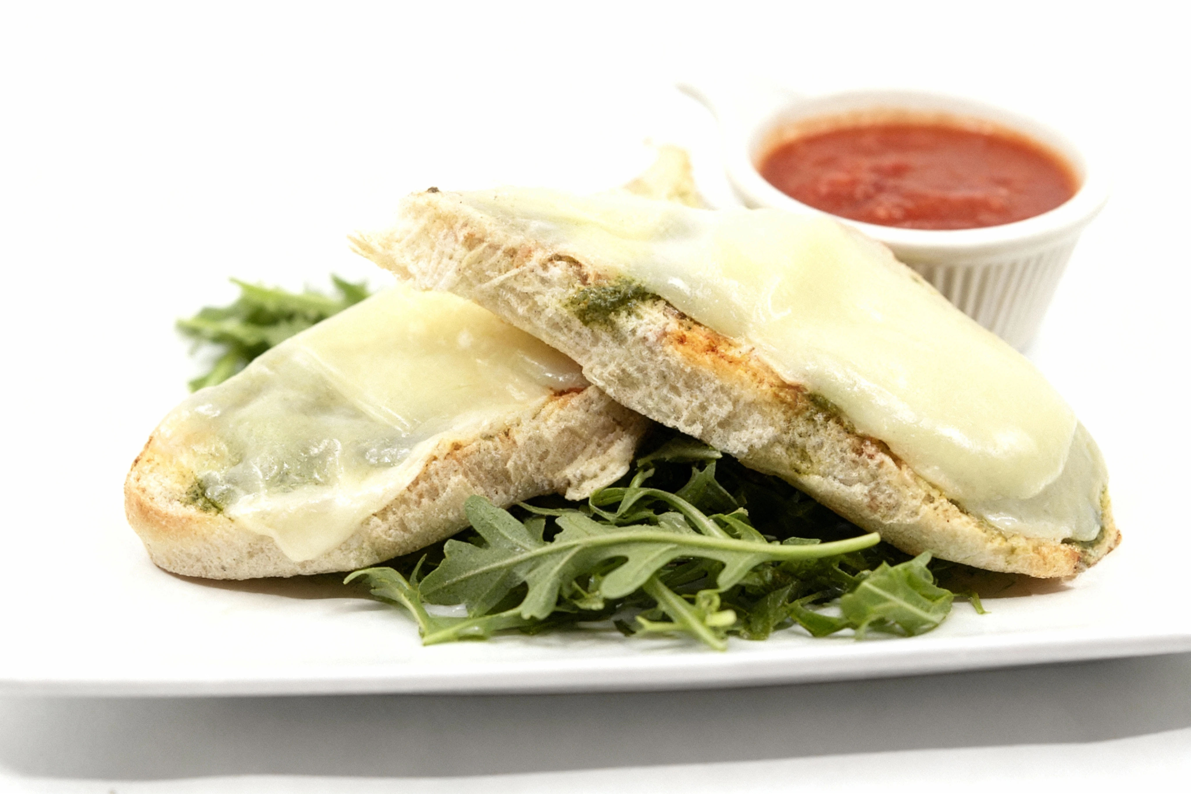 Toasted bread slices topped with melted mozzarella cheese and pesto, served on a bed of fresh arugula with a side of marinara sauce.
