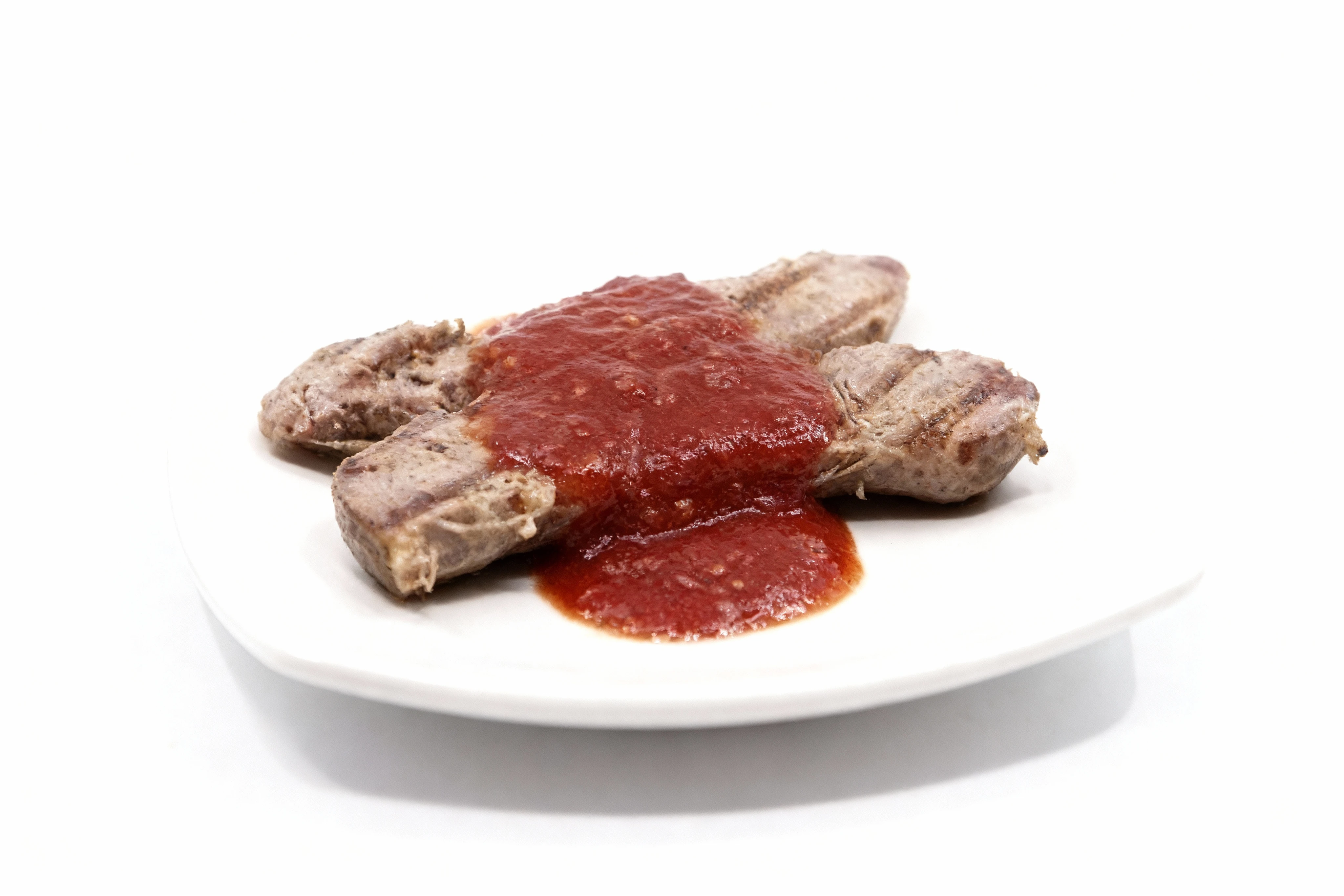 Two grilled sausages served on a white plate and topped with chunky tomato sauce.