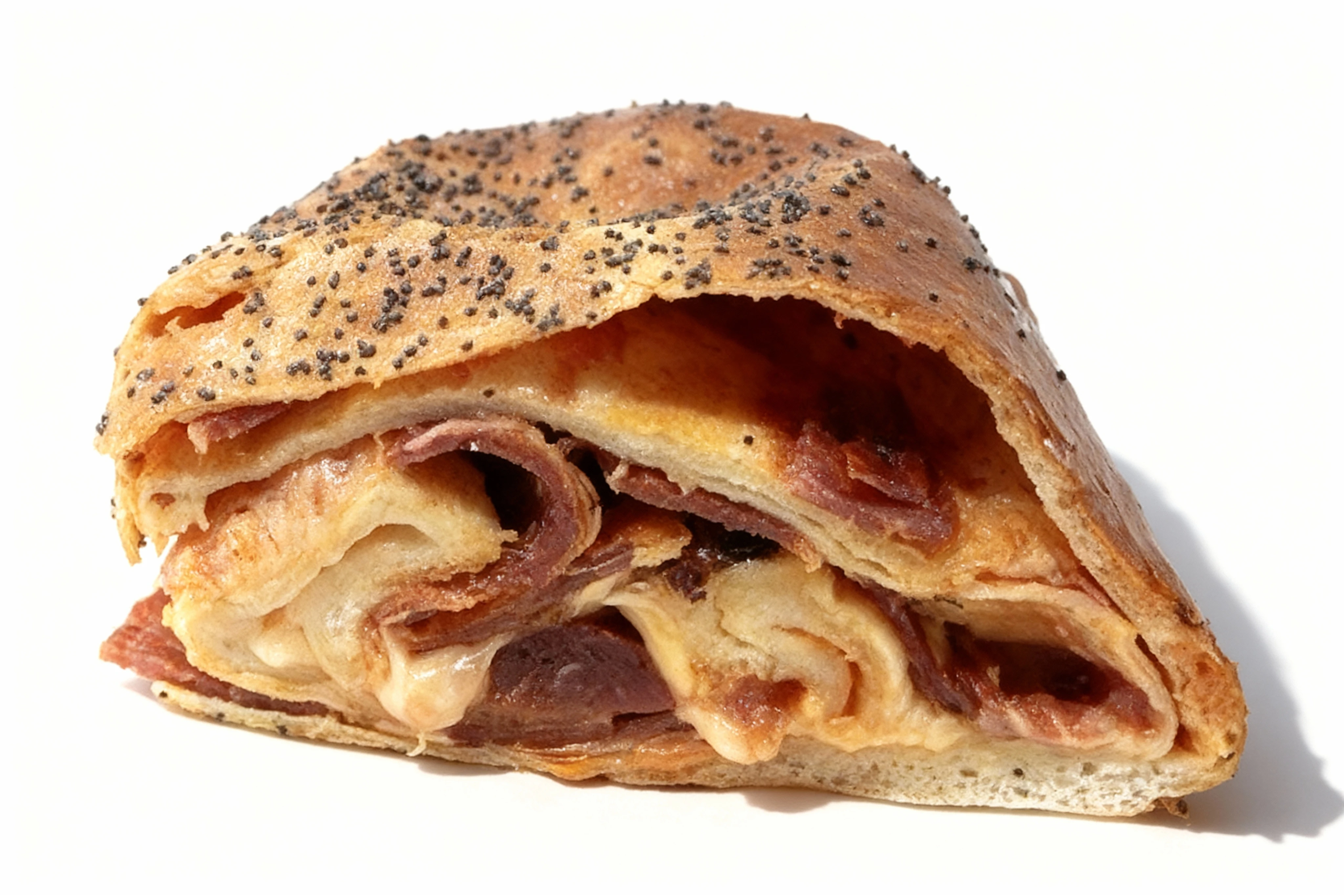 A cross-section of a savory stromboli or meat-filled roll containing layers of sliced ham or pepperoni and melted cheese, topped with poppy seeds.