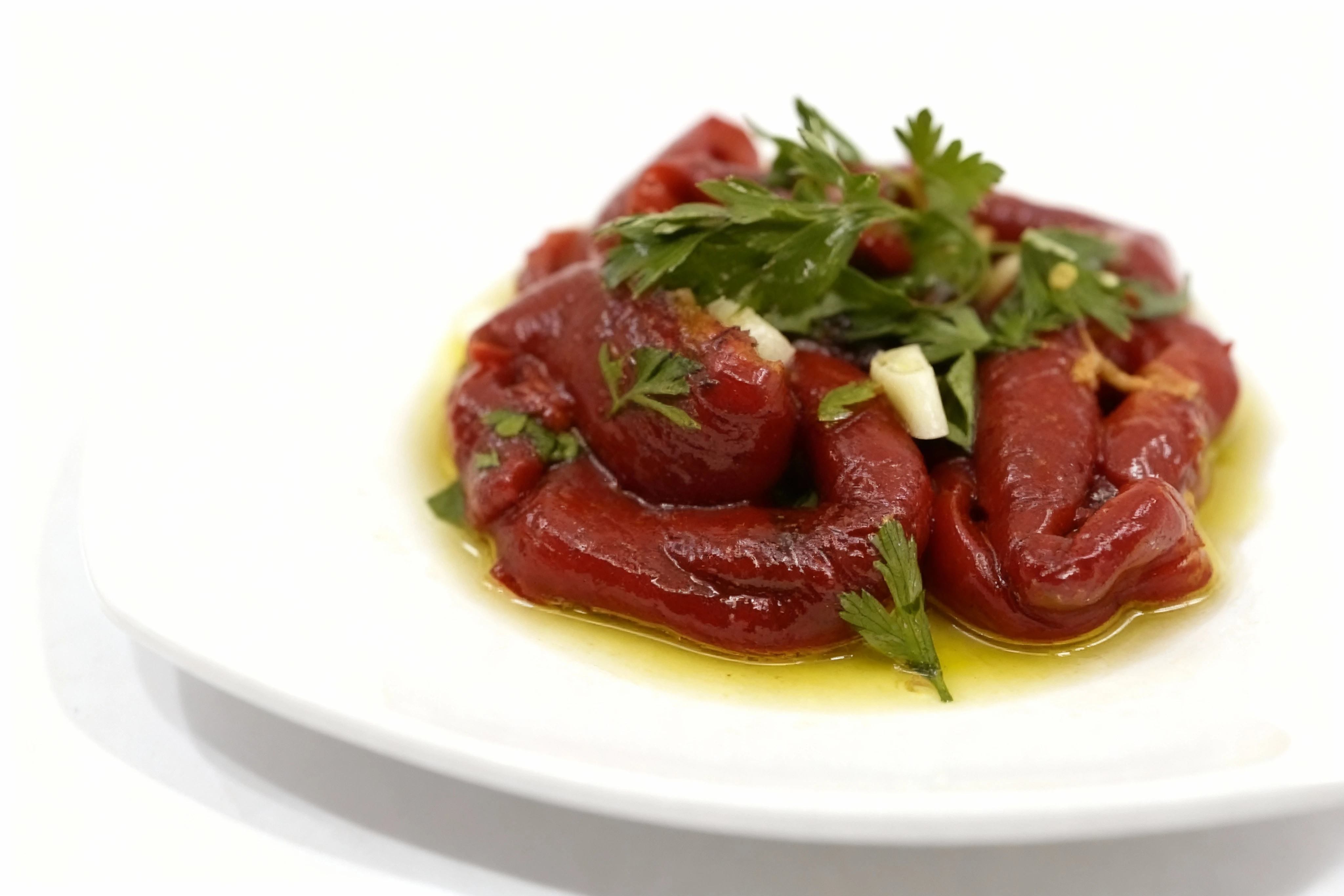 Roasted red peppers marinated in olive oil, topped with sliced garlic and fresh parsley leaves.