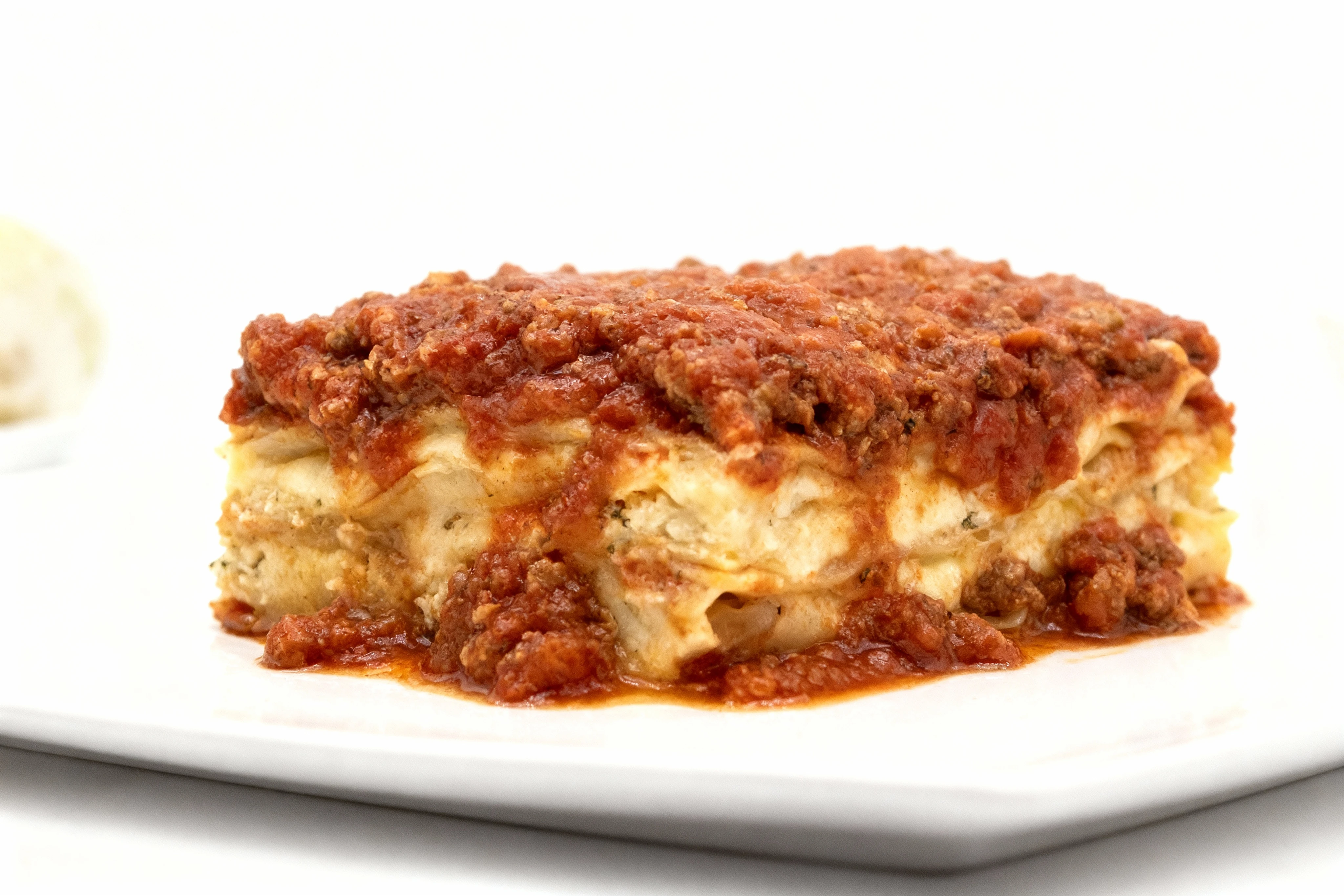 A square slice of baked lasagna featuring layers of pasta and ricotta cheese topped with a thick meat sauce.