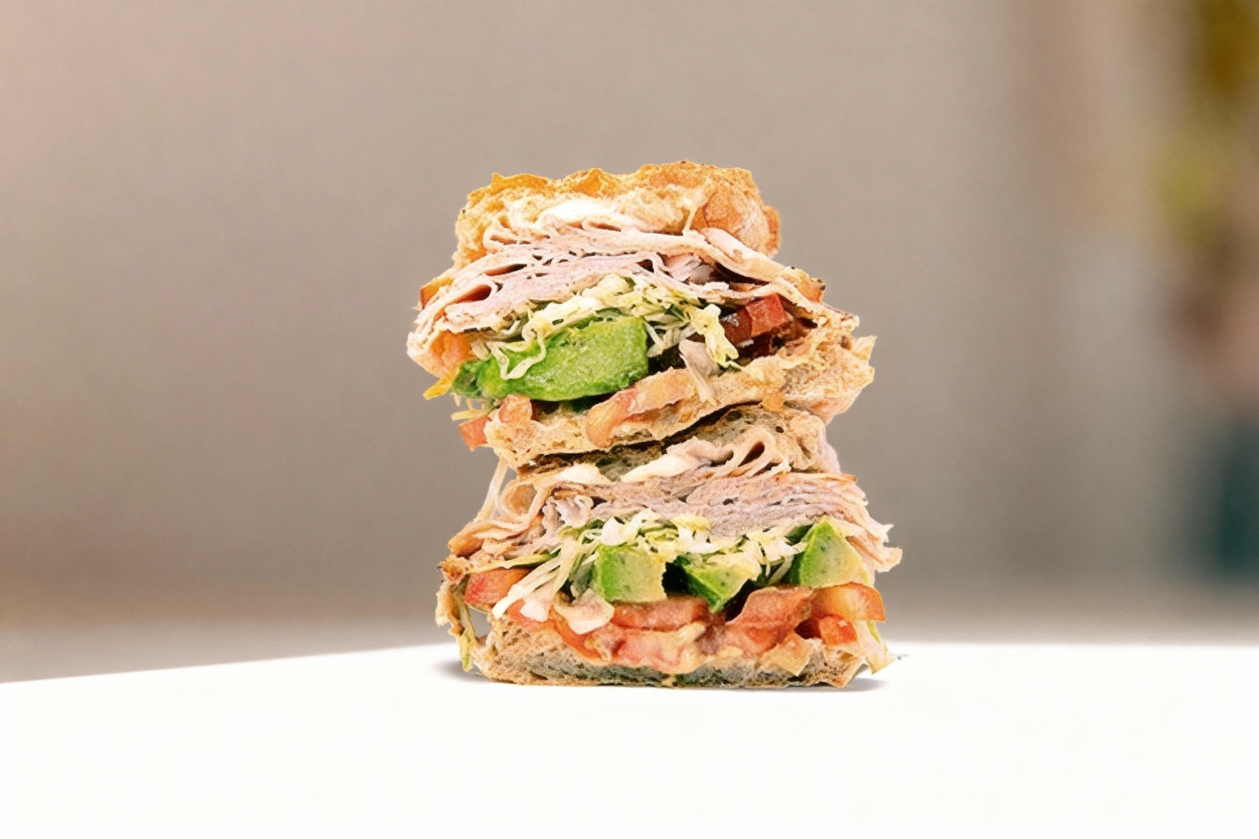 A stacked sandwich cut in half featuring layers of sliced deli turkey, thick avocado chunks, shredded lettuce, and diced tomatoes on a crusty roll.