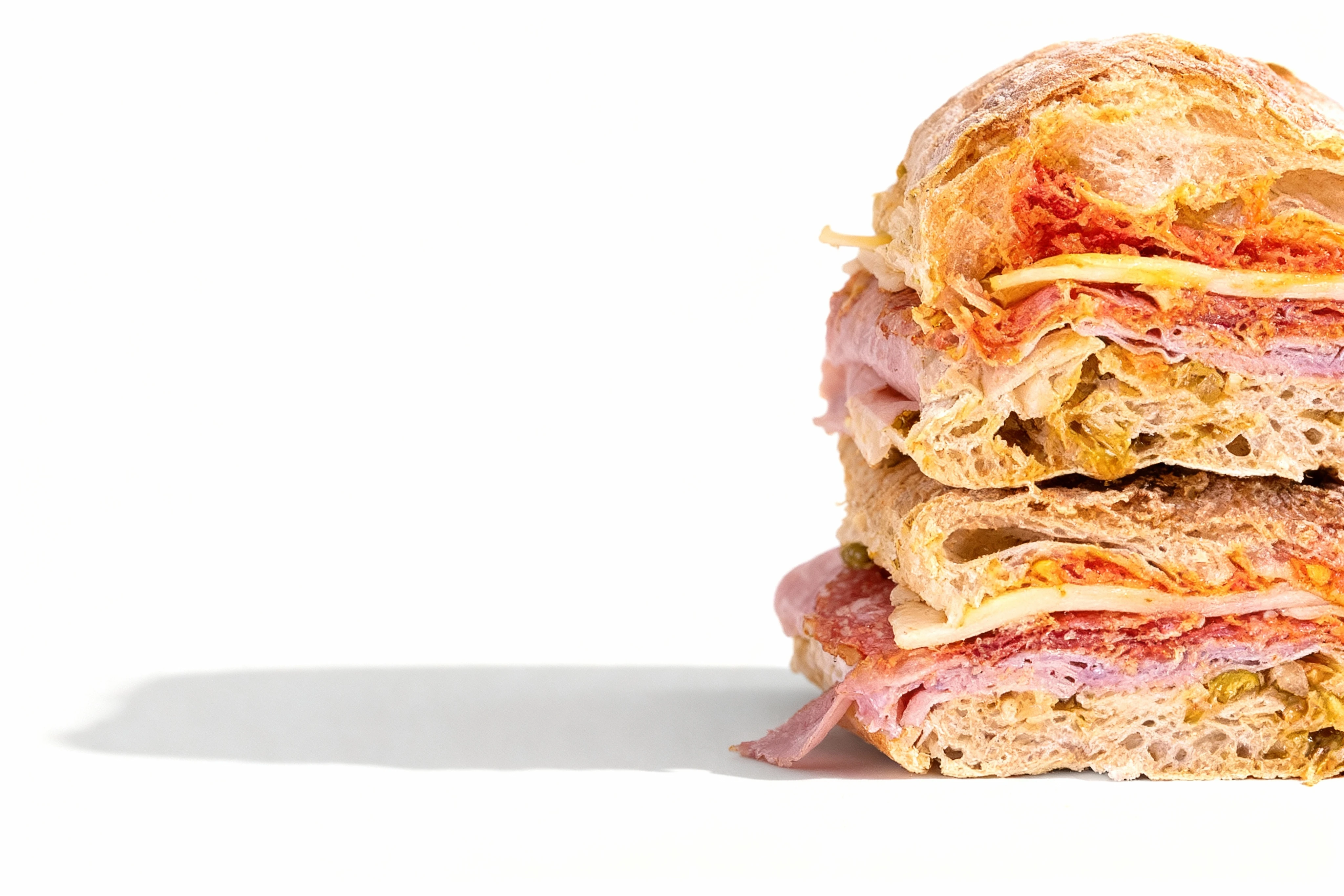 A stacked ciabatta sandwich featuring layers of sliced ham, salami, provolone cheese, and olive giardiniera.