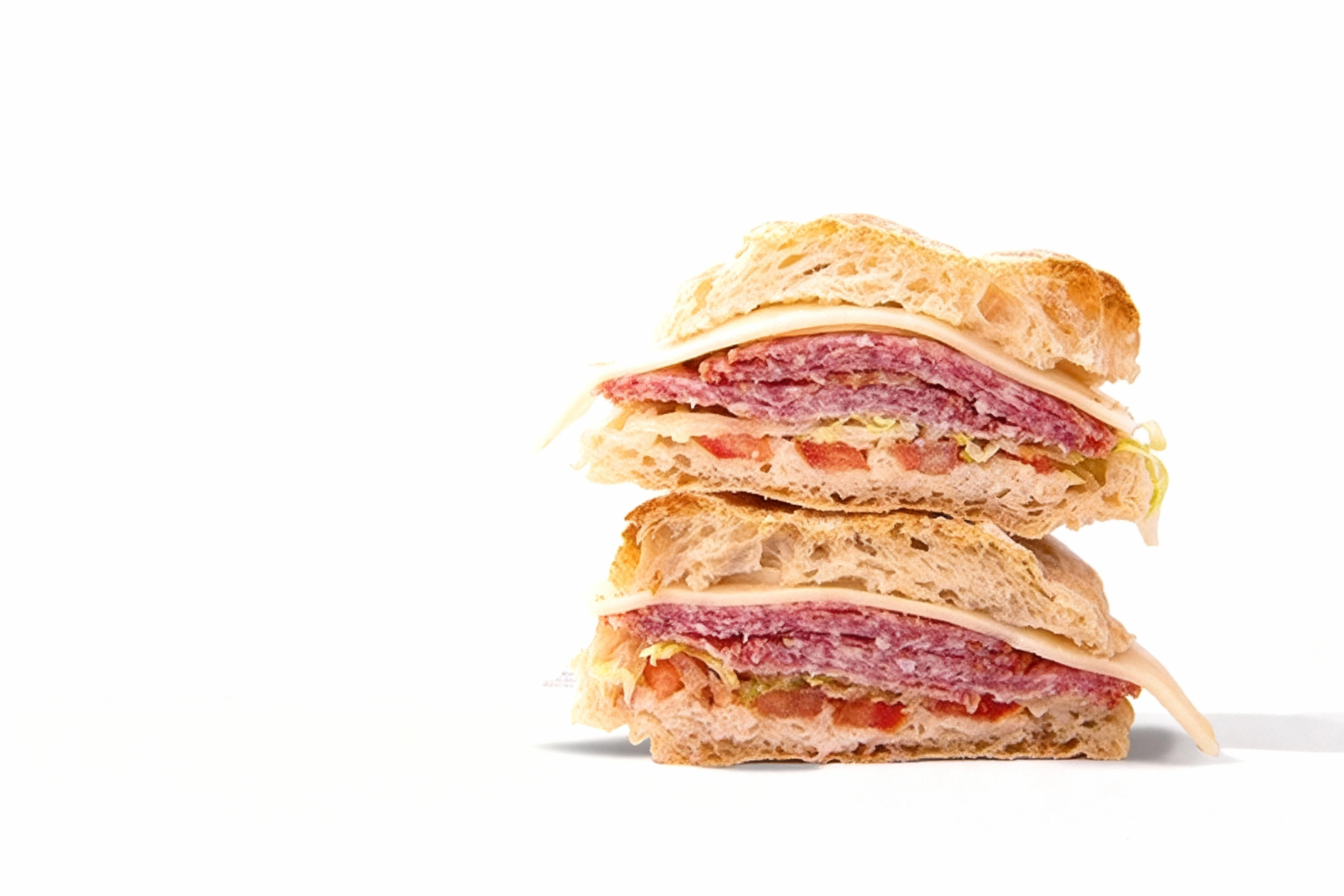 A stacked ciabatta sandwich filled with layers of sliced salami, provolone cheese, lettuce, and chopped tomatoes.