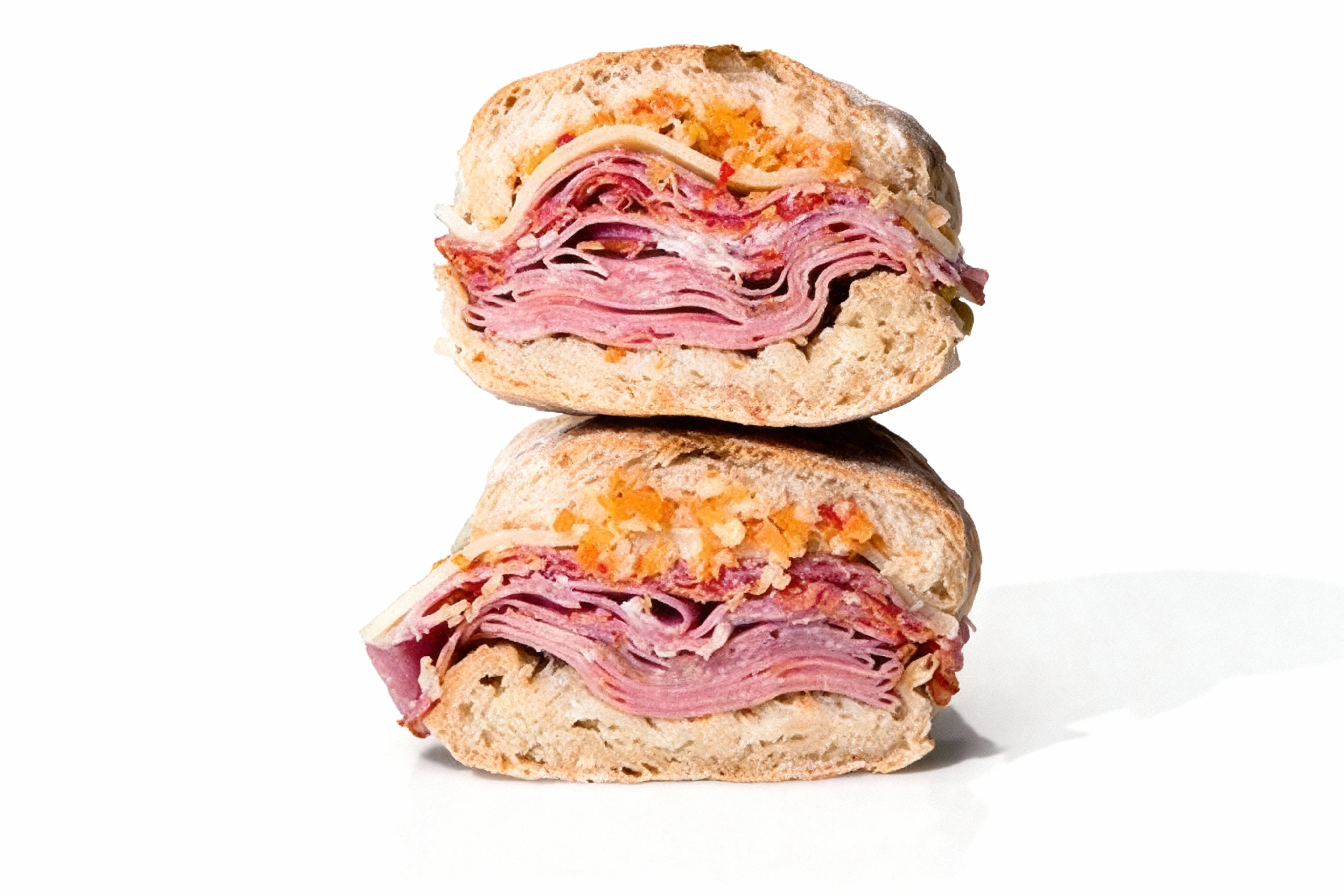 Muffuletta sandwich halves stacked on each other, filled with layers of sliced salami, ham, mortadella, provolone cheese, and olive salad on crusty bread.