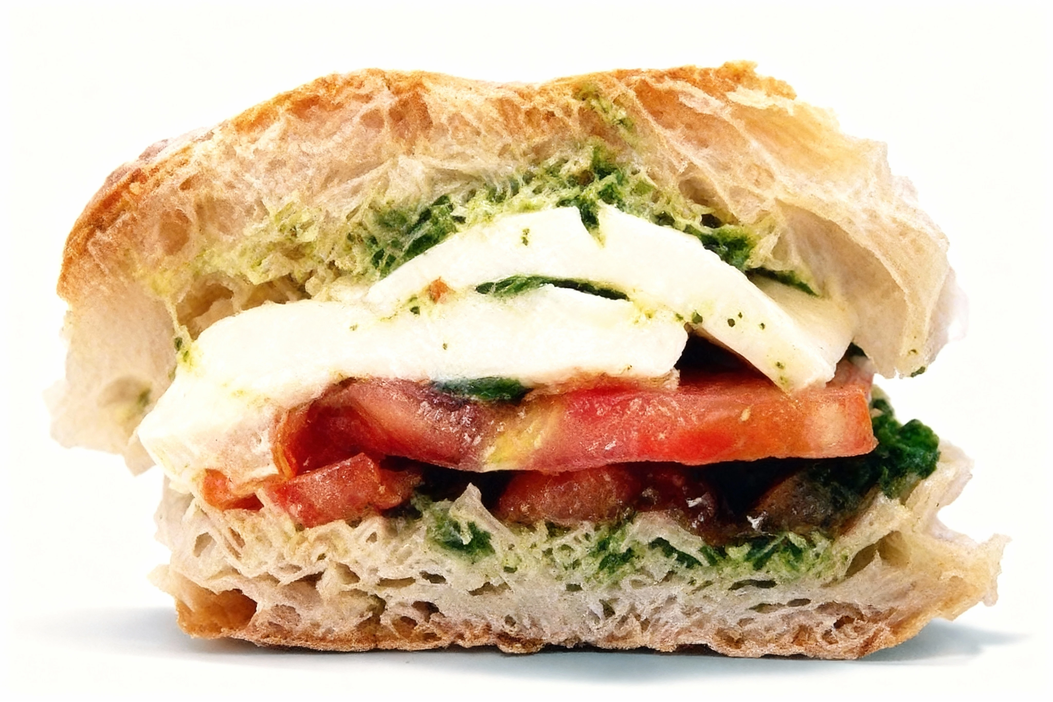 A caprese panini featuring sliced fresh mozzarella, ripe tomato slices, and green pesto on crusty ciabatta bread.