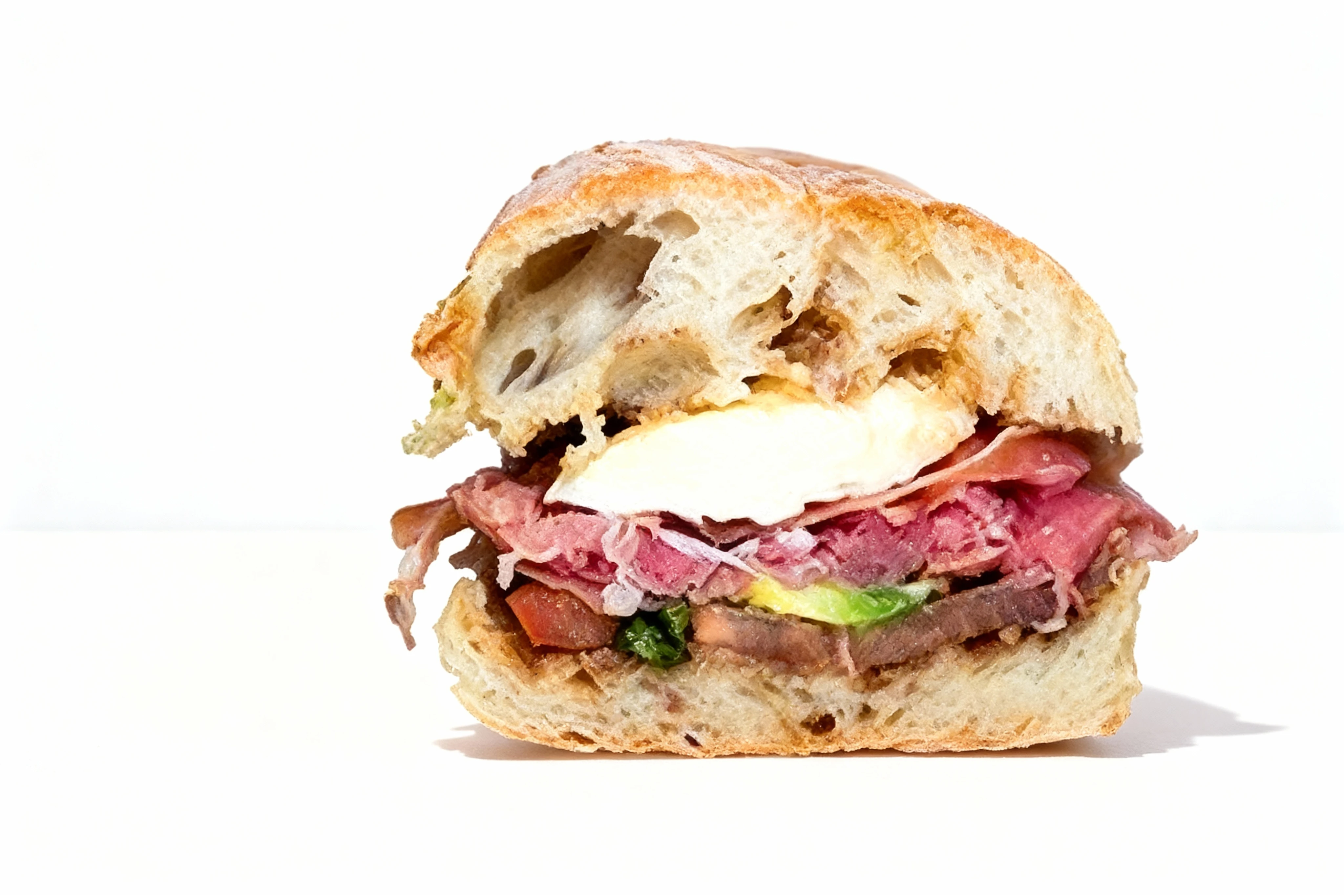 A sandwich on a crusty baguette featuring thin slices of roast beef, fresh mozzarella, tomato, and greens.