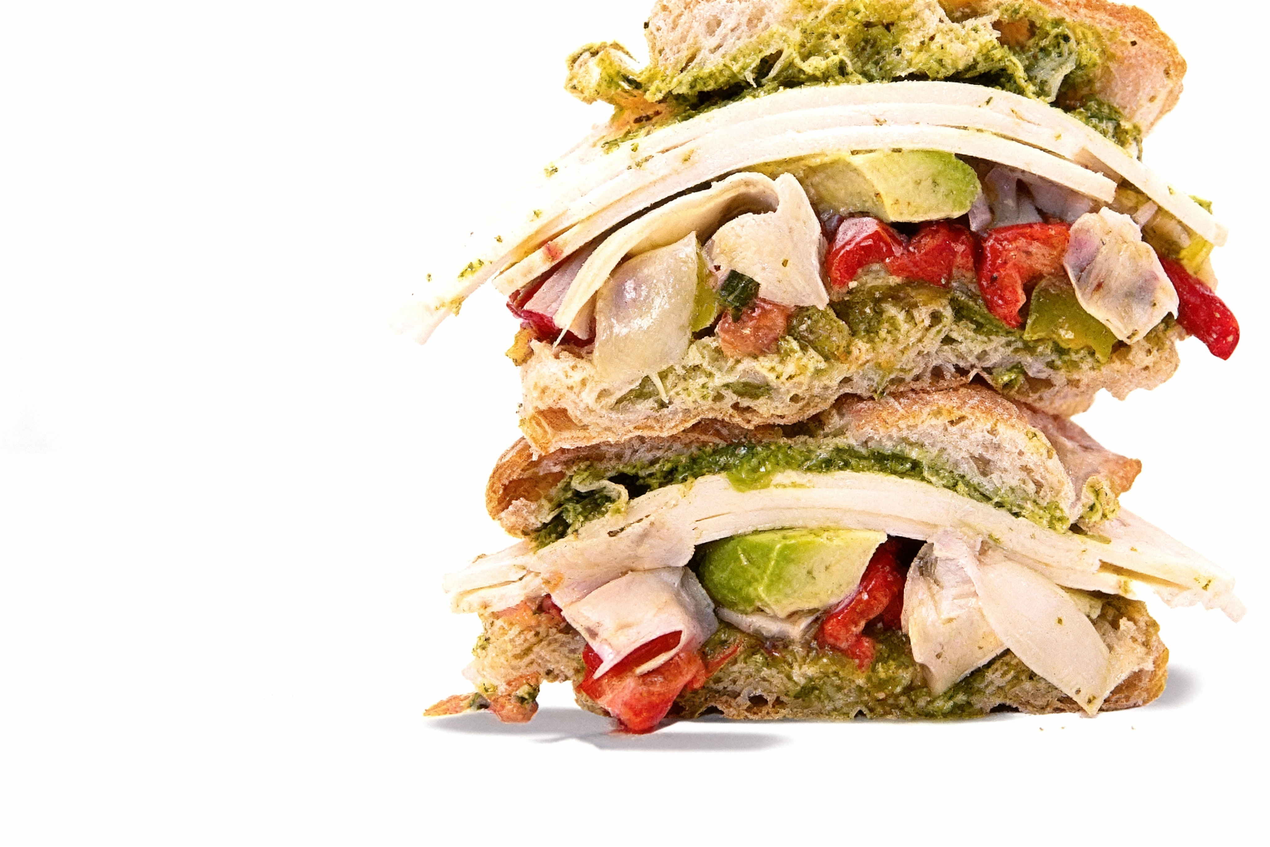 A stacked ciabatta sandwich filled with sliced deli turkey, avocado wedges, roasted red peppers, artichoke hearts, and pesto sauce.