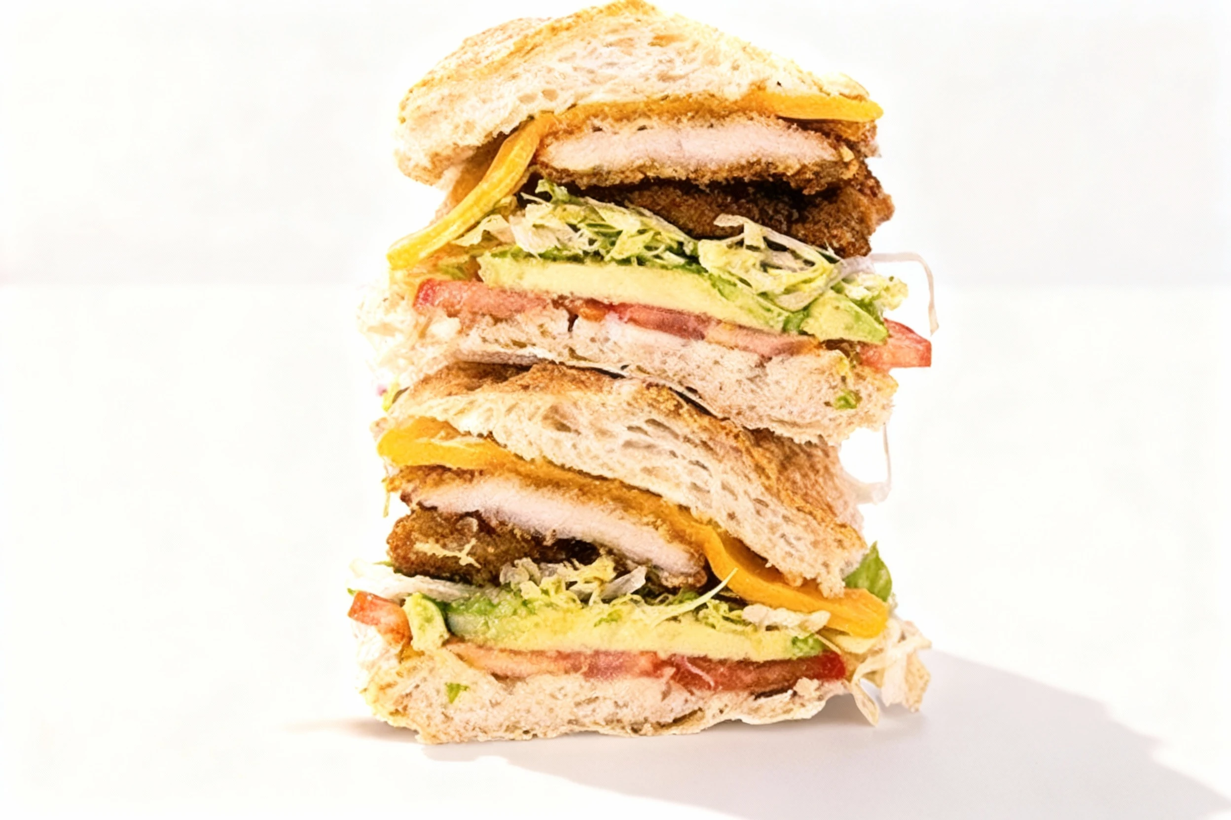 A stacked breaded chicken torta sandwich on a crusty roll with sliced avocado, fresh tomatoes, shredded lettuce, and melted yellow cheese.