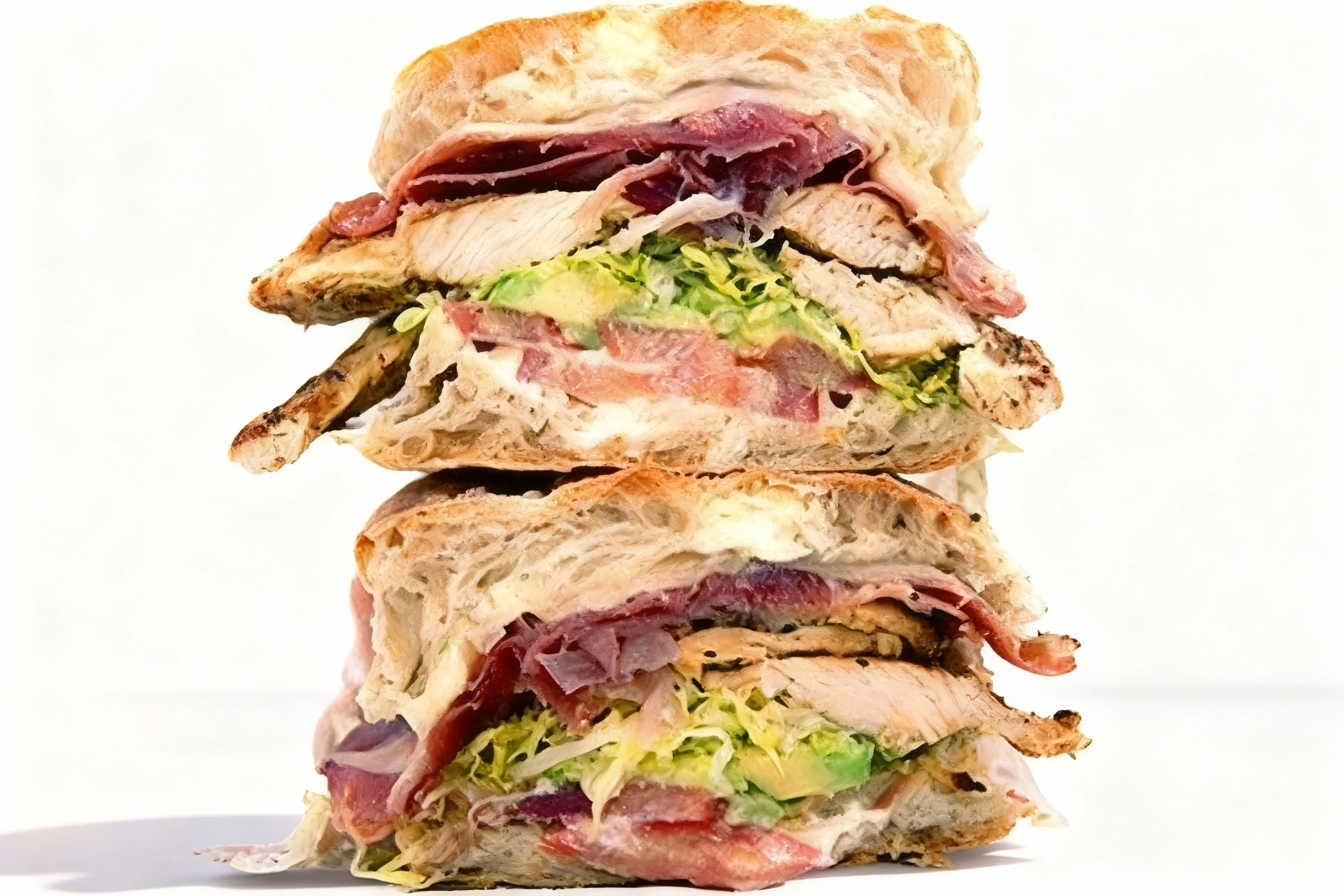 A stacked ciabatta sandwich featuring grilled chicken breast, sliced ham, shredded lettuce, tomatoes, and avocado.