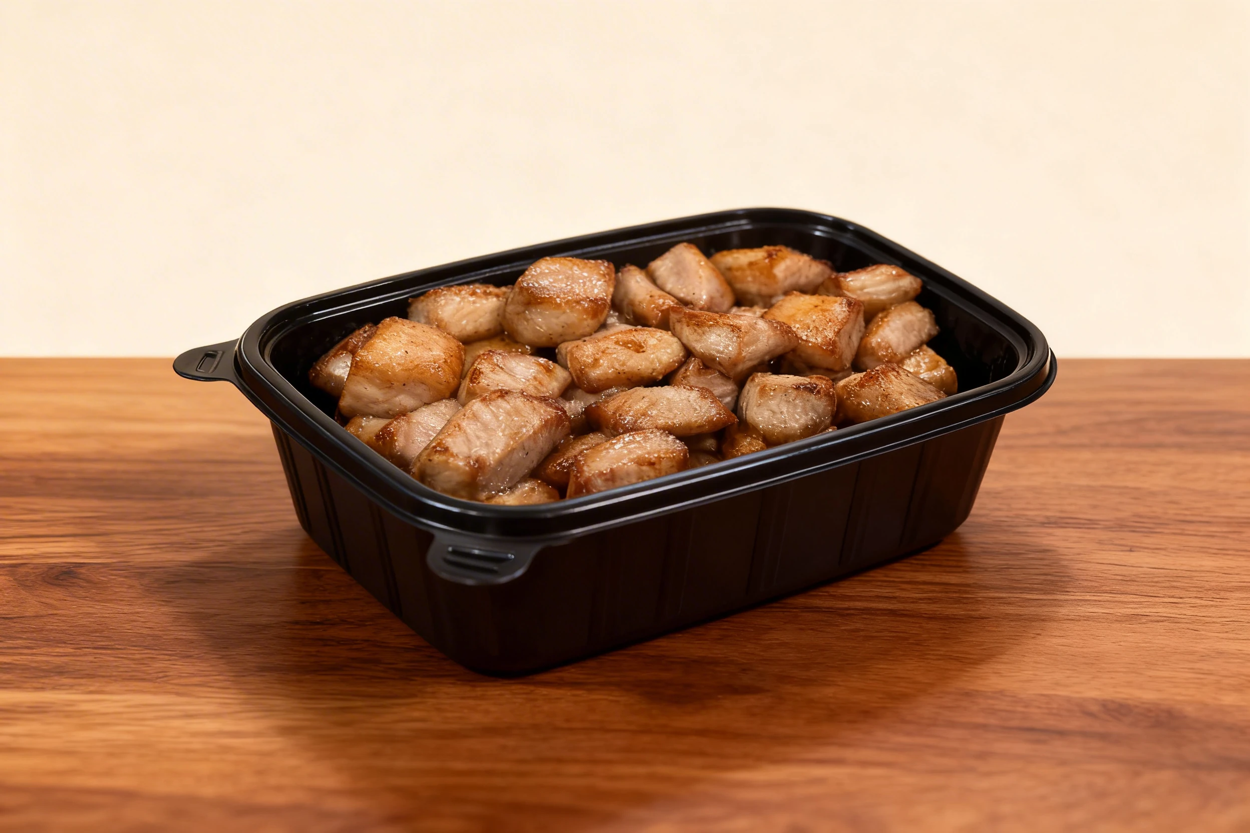 Seared pork belly or chicken breast cubes served inside a black plastic takeaway container.
