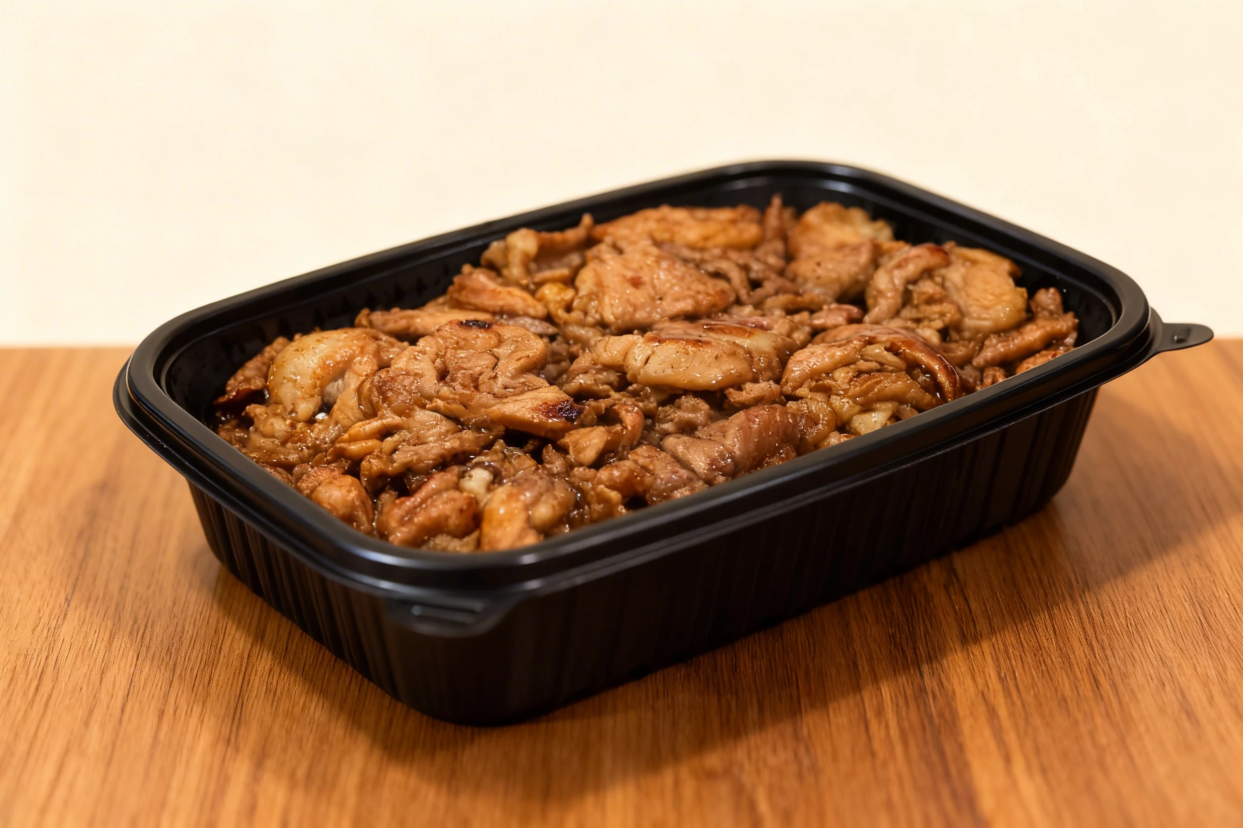 Grilled thinly sliced pork or beef with a savory glaze, served in a black plastic takeaway container.