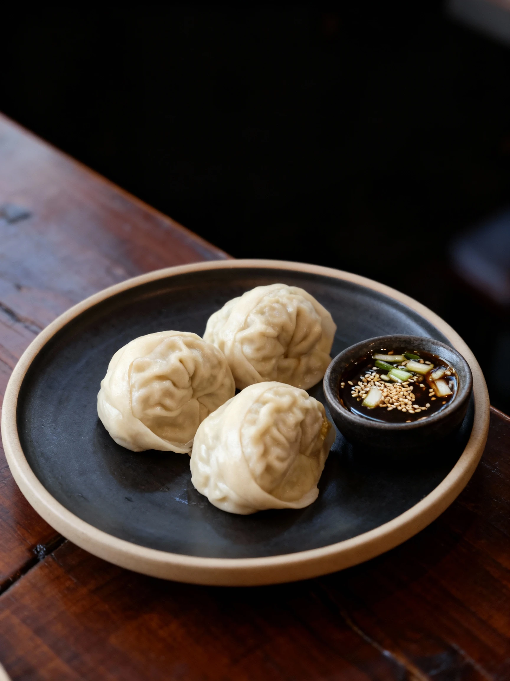 Four large steamed Mandu dumplings served on a black textured plastic tray with a built-in sauce compartment.