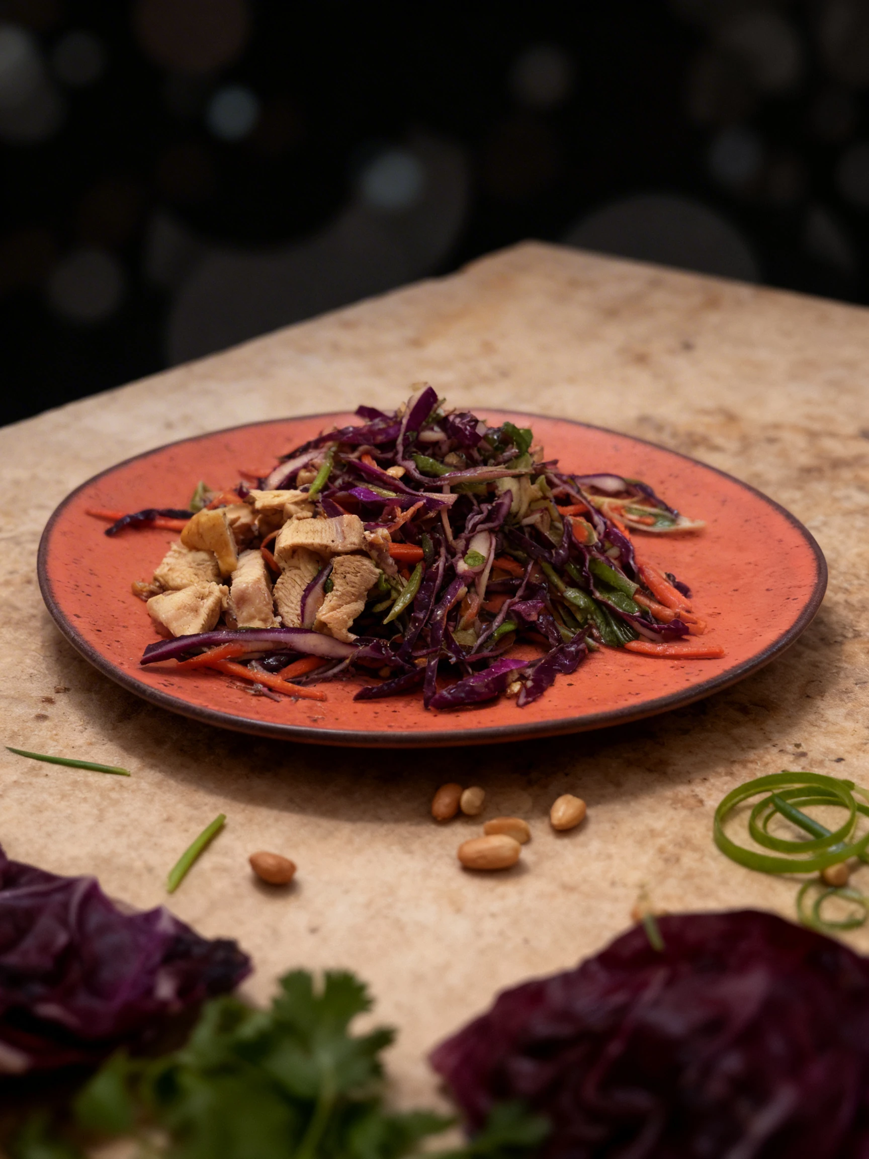 A chicken salad with sliced grilled chicken breast, shredded red cabbage, carrots, green onions, and peanuts on a terracotta-colored plate.