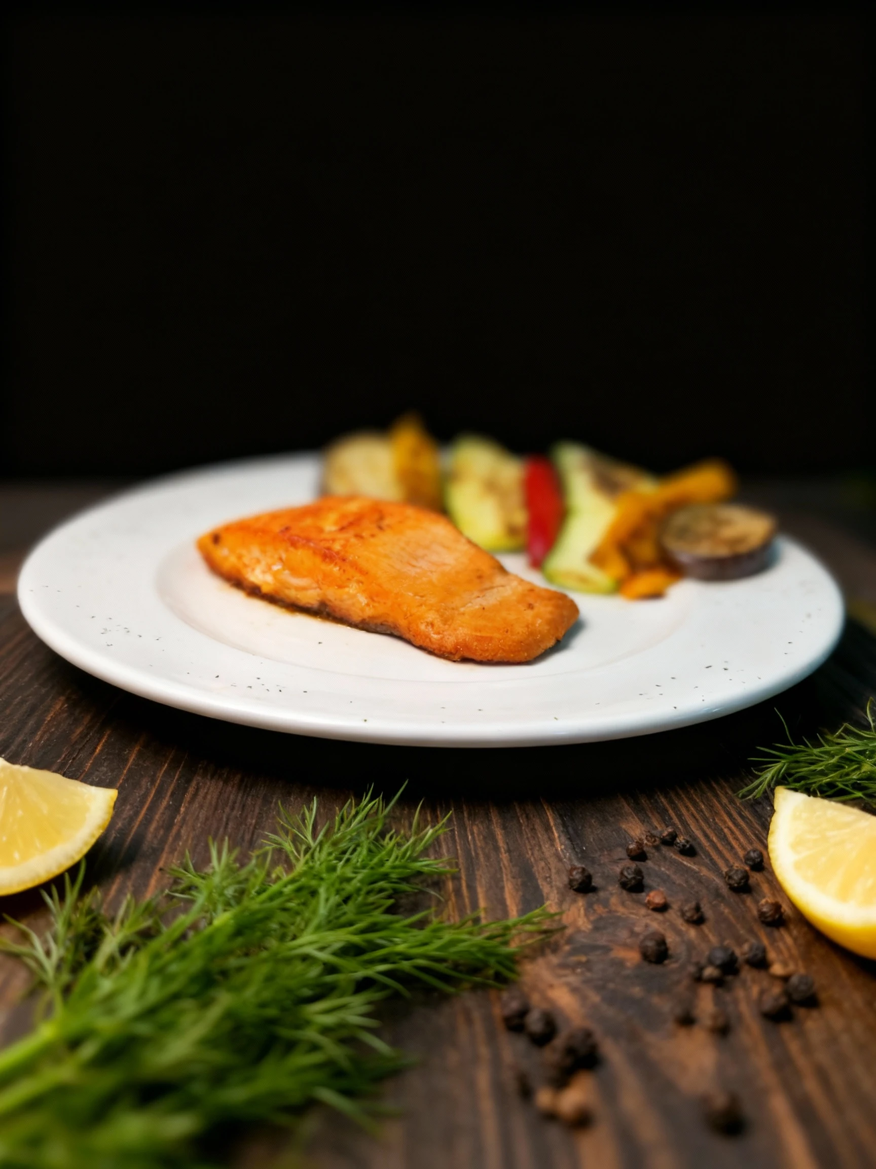 A seared salmon fillet served on a white plate with a side of grilled vegetables, including zucchini slices, eggplant, and red bell peppers.