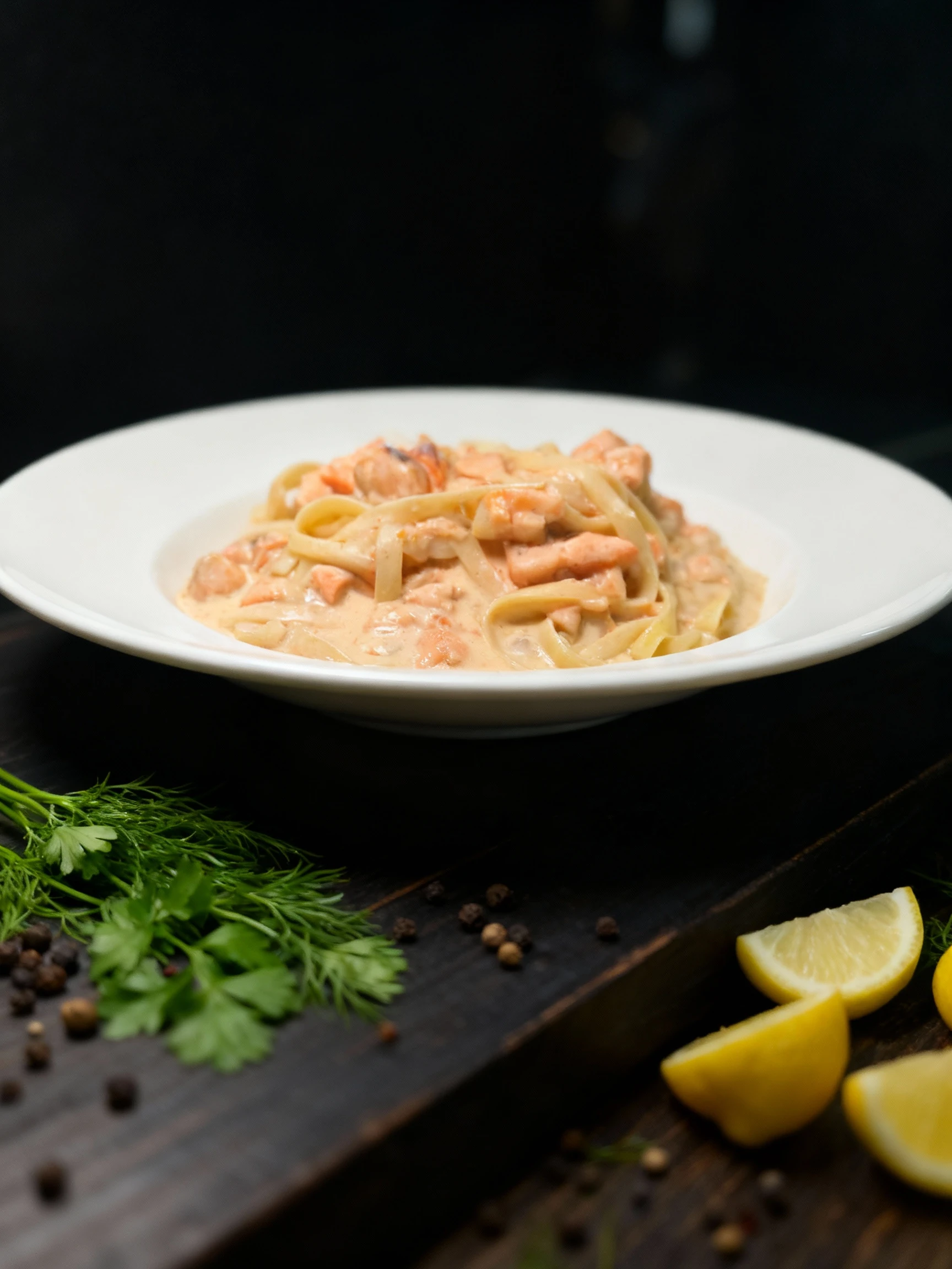 Tagliatelle pasta with chunks of cooked salmon in a creamy pink sauce, served in a wide-rimmed white bowl.