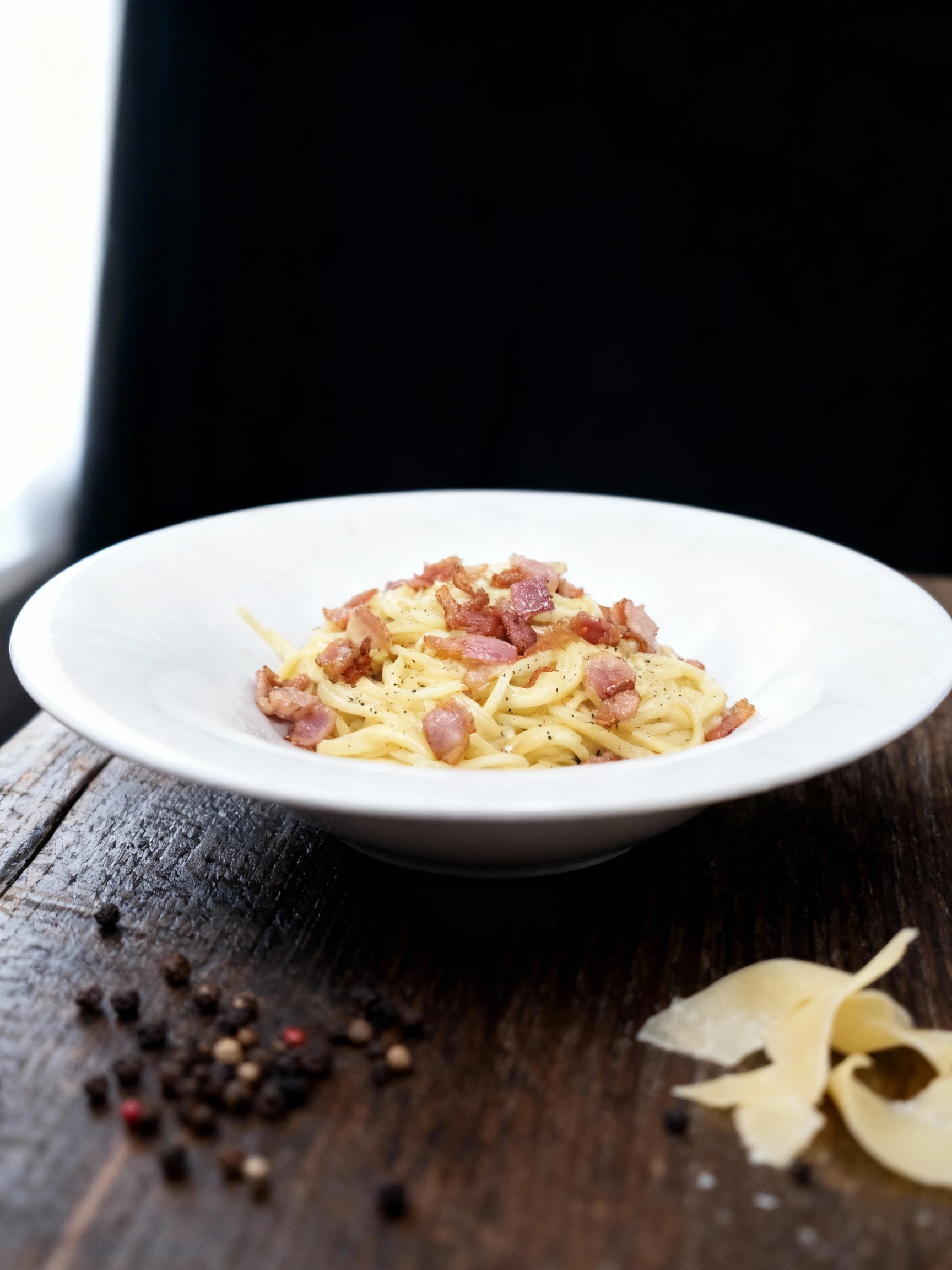 Spaghetti alla carbonara featuring long pasta coated in a creamy egg and cheese sauce, topped with pieces of crispy guanciale and cracked black pepper.