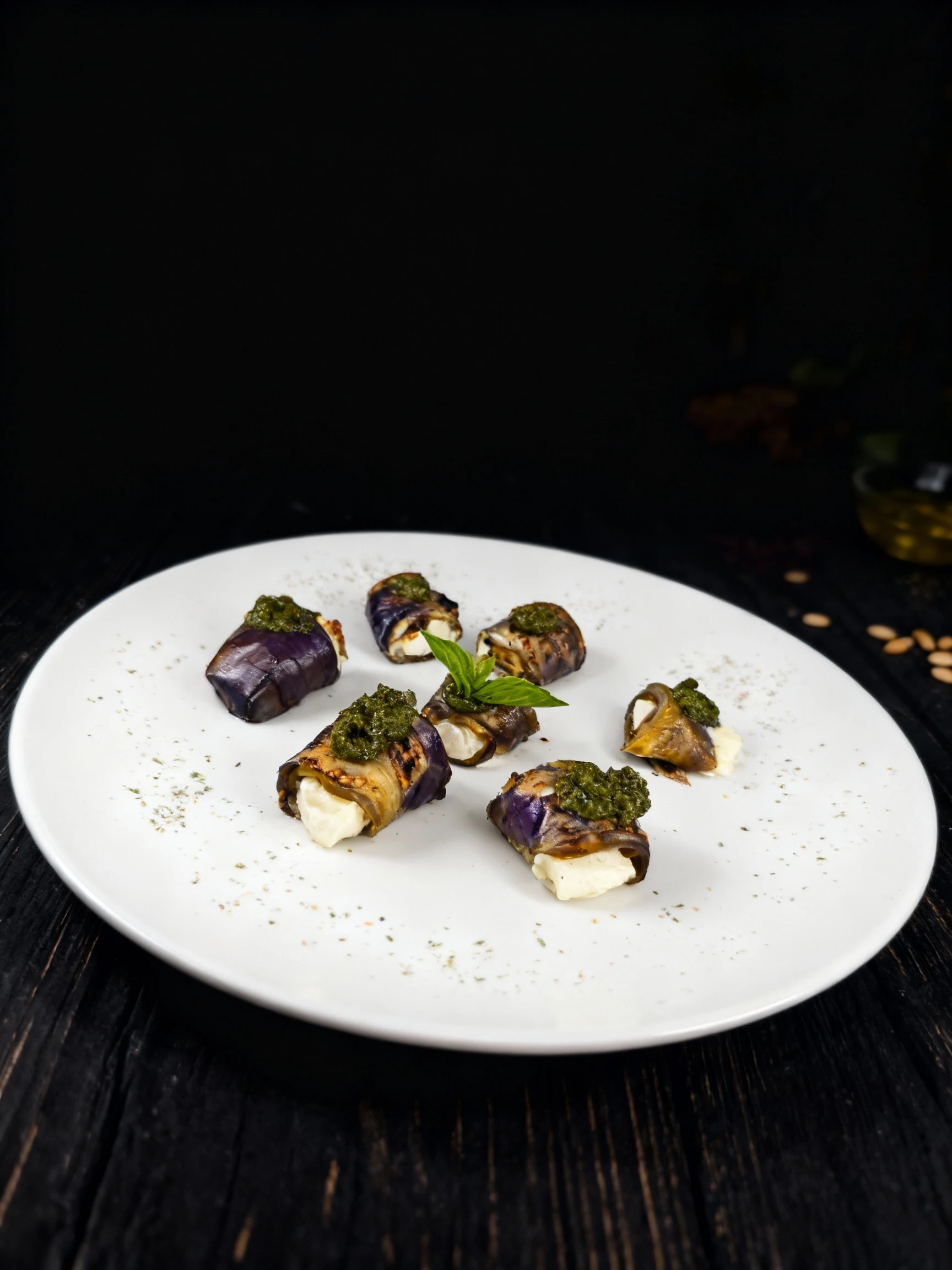Grilled eggplant rolls filled with soft white cheese, topped with green pesto and a garnish of fresh basil leaves.