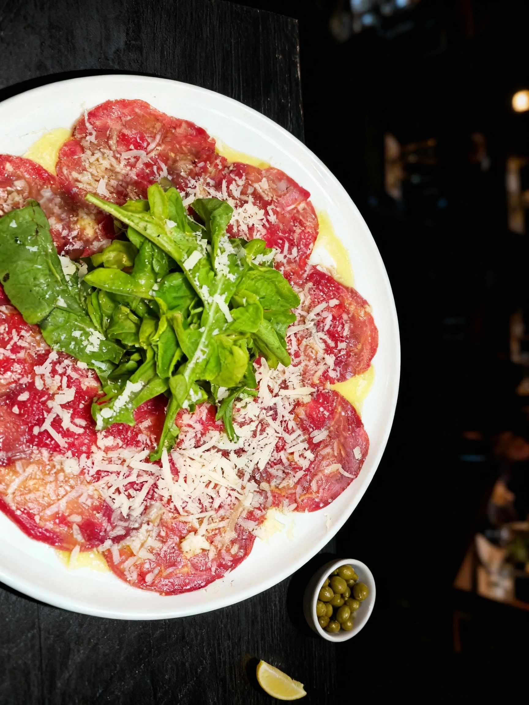 Beef carpaccio featuring thinly sliced raw beef topped with a mound of fresh arugula, grated parmesan cheese, and a drizzle of olive oil.