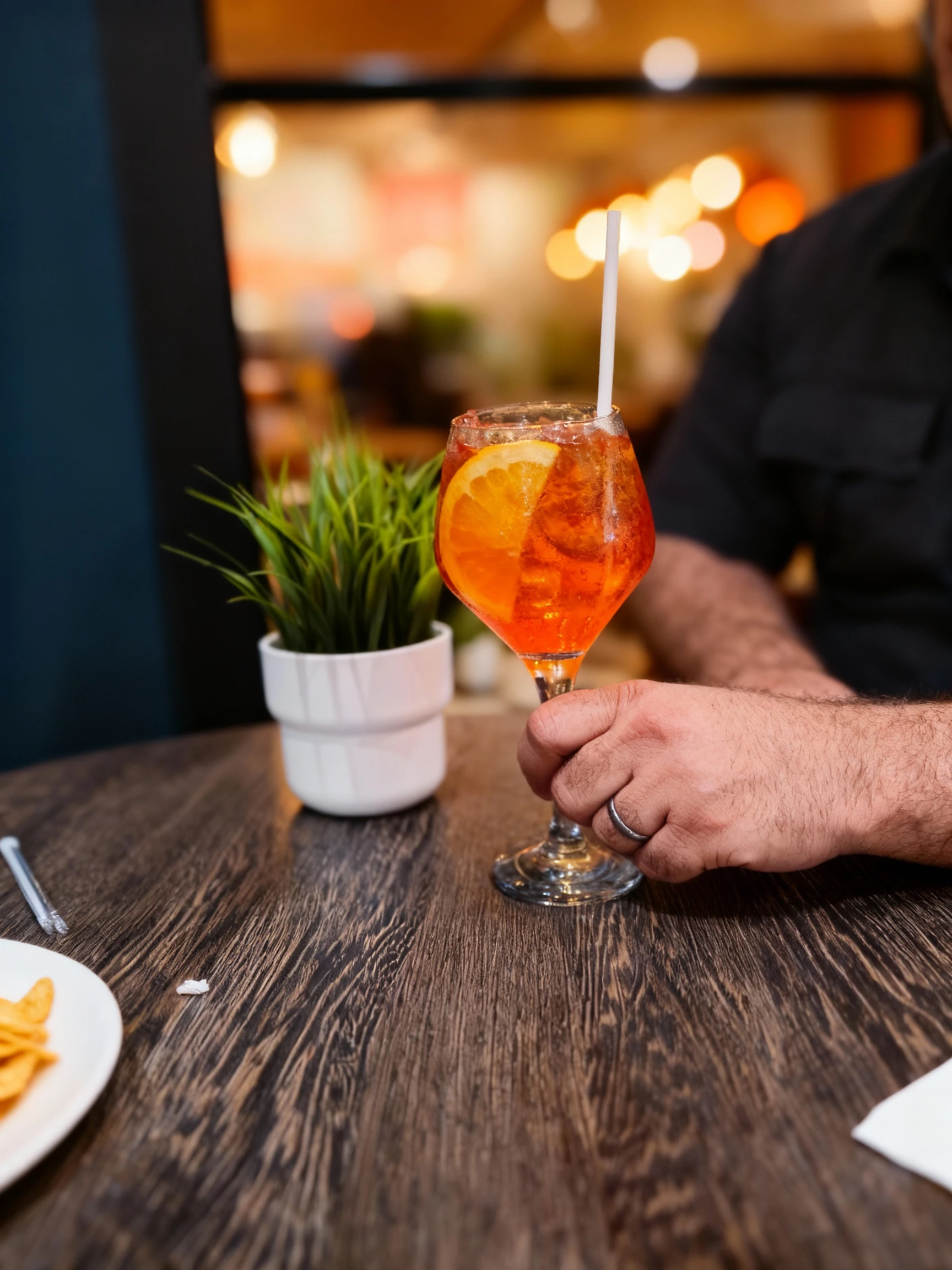 An Aperol Spritz cocktail served in a large wine glass with ice, a fresh orange slice, and a white plastic straw.