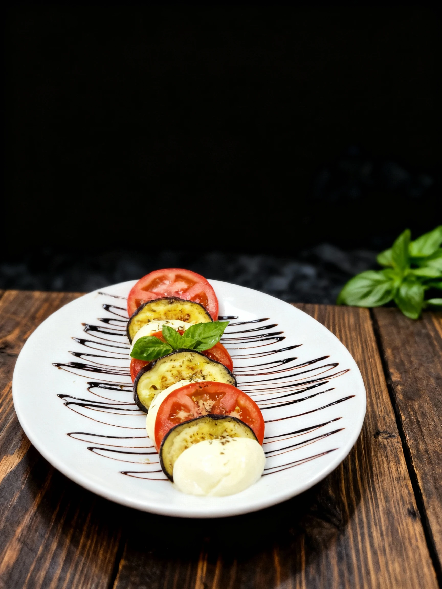 Caprese-style salad featuring alternating slices of fresh tomato, grilled eggplant, and mozzarella cheese drizzled with balsamic glaze and topped with fresh bas