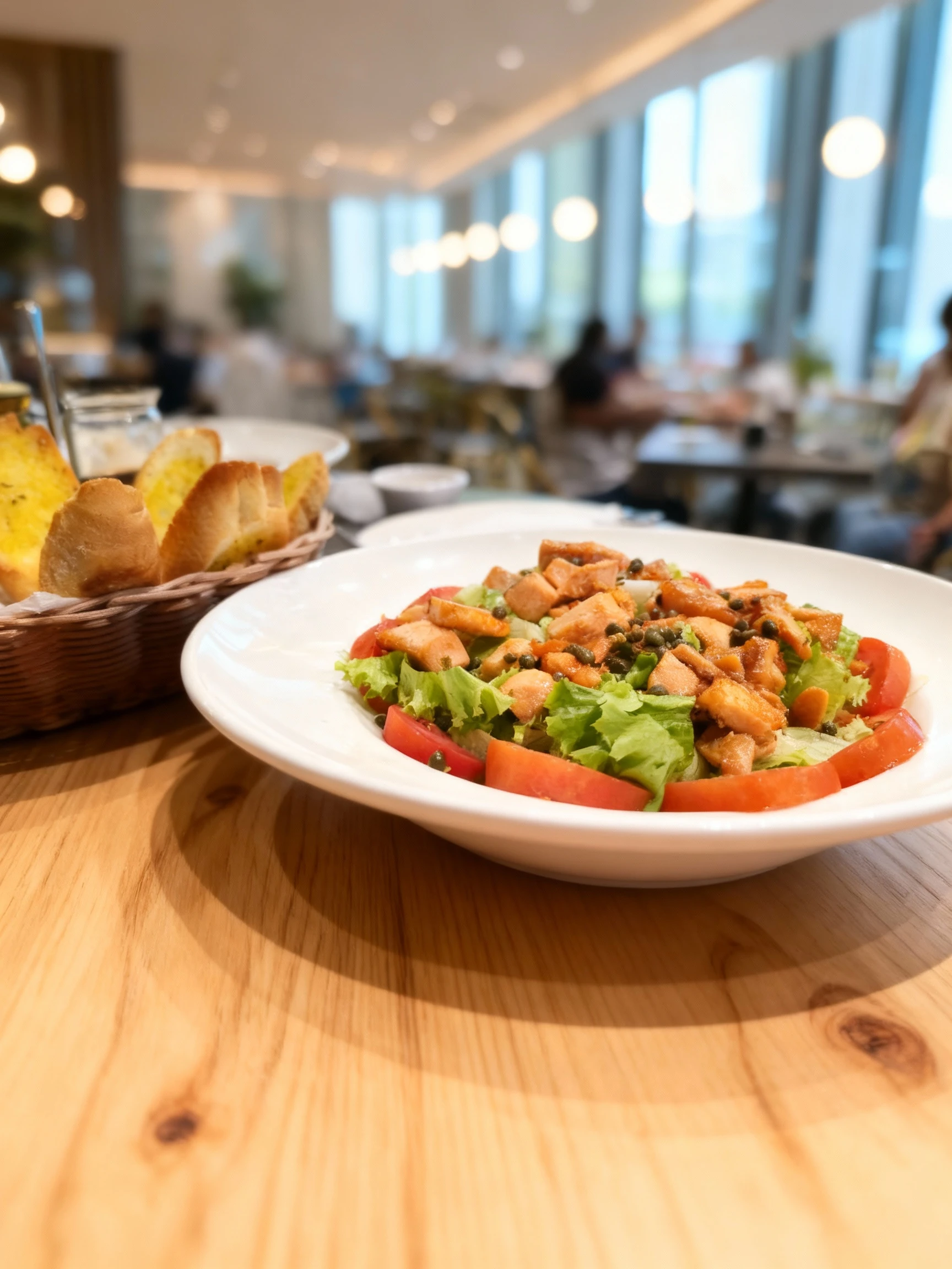 A salmon salad featuring seared salmon chunks and capers over fresh lettuce and sliced tomatoes, served with a side of toasted garlic bread pieces.