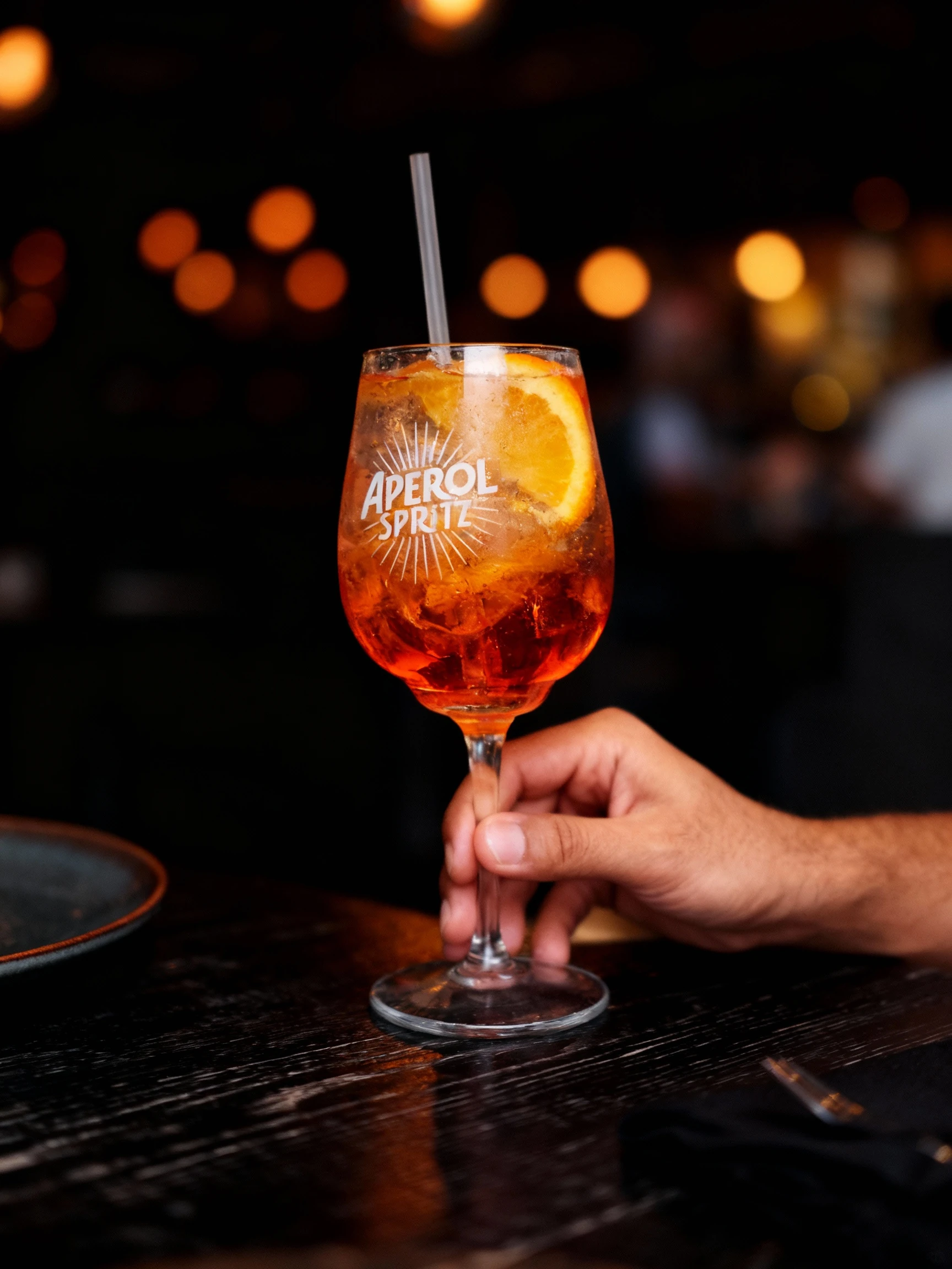An Aperol Spritz cocktail served with ice cubes and an orange slice in a branded wine glass.