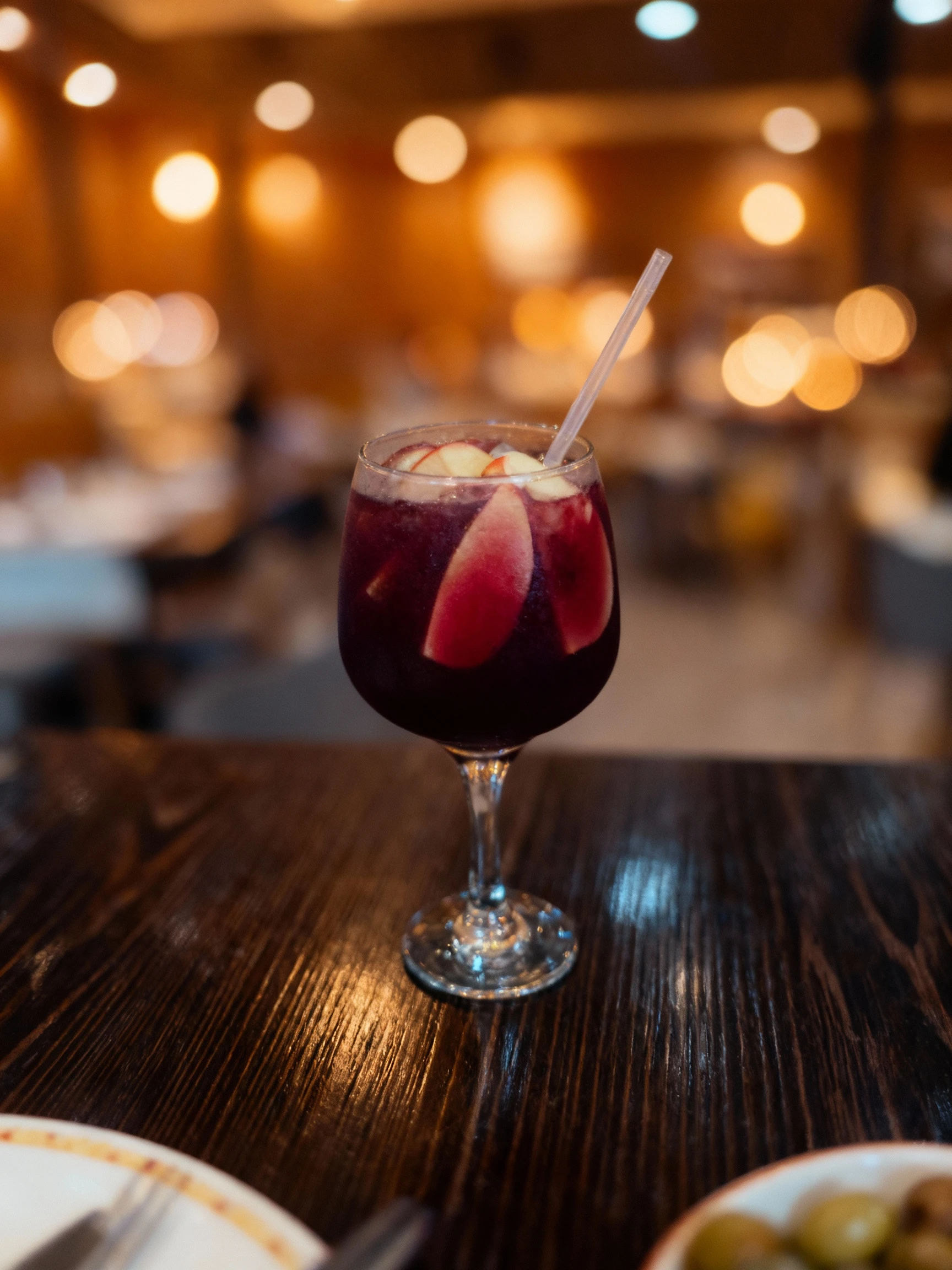 A glass of red wine sangria featuring thin apple slices and a clear plastic straw.