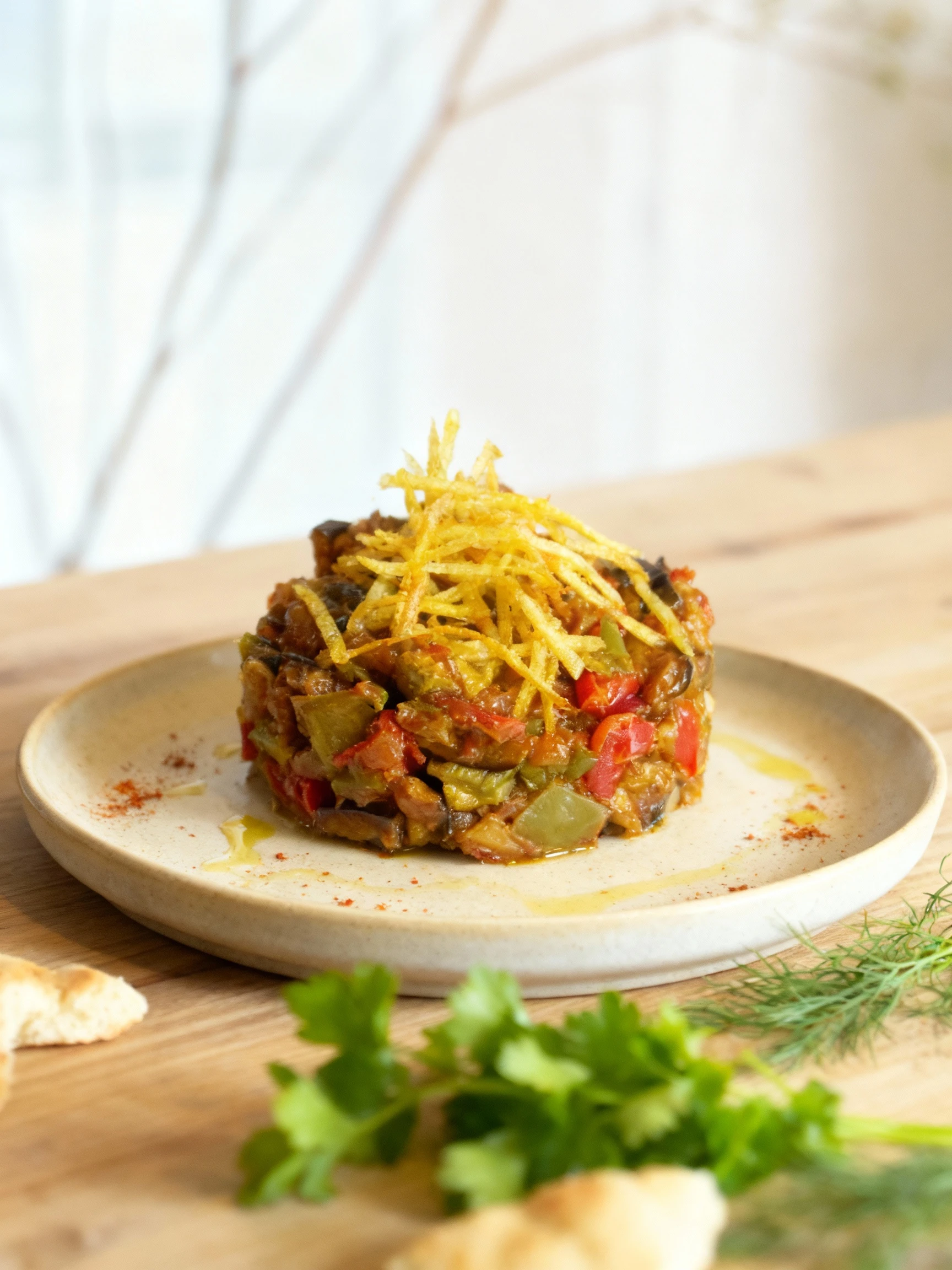 A molded serving of stewed vegetables, featuring chopped eggplant, red peppers, and green peppers in a rich sauce, garnished with a nest of crispy, golden shoes
