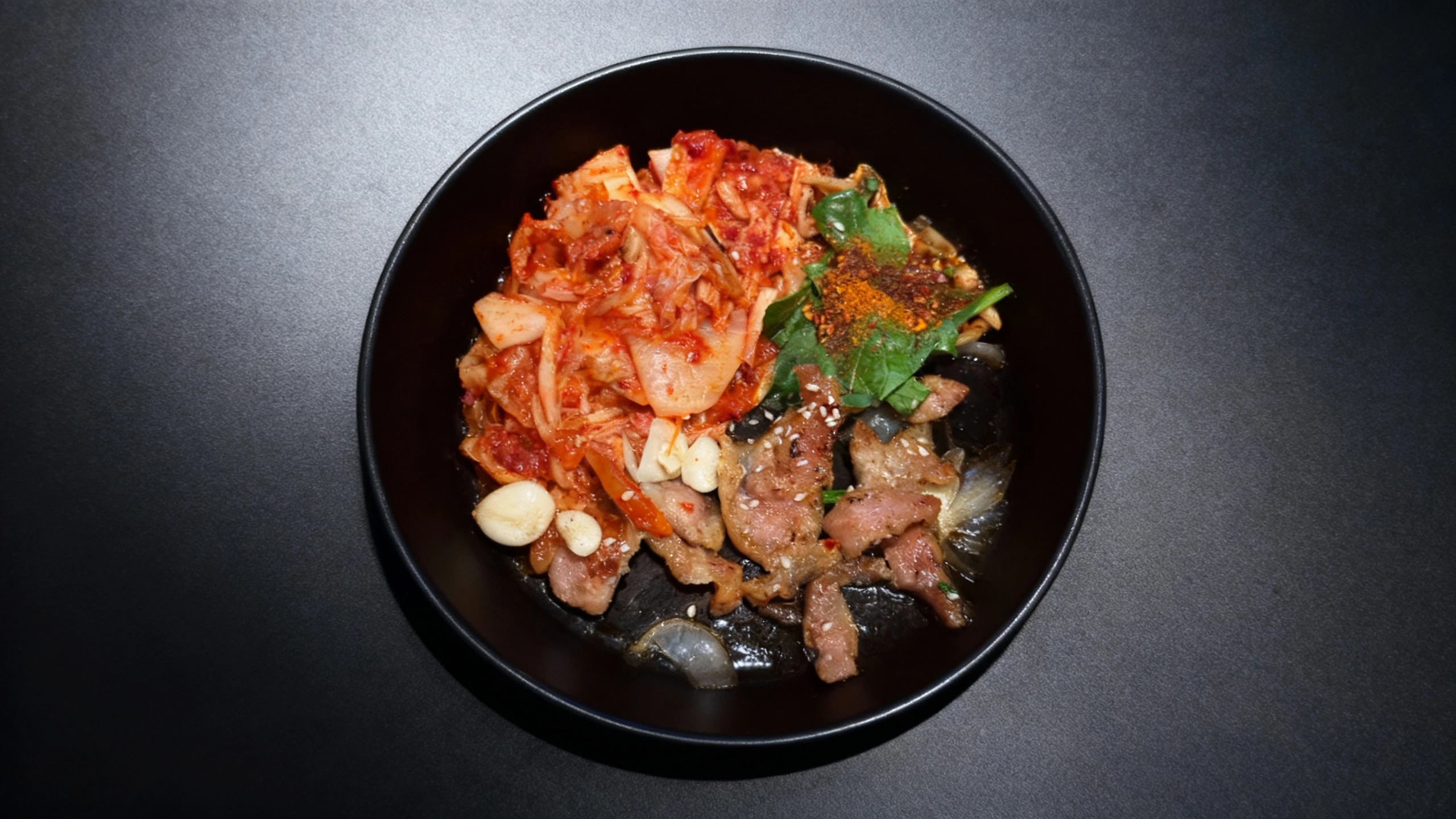 A close-up of a stir-fried dish featuring thin slices of seared meat garnished with sesame seeds, served alongside a pile of spicy fermented kimchi with whole g