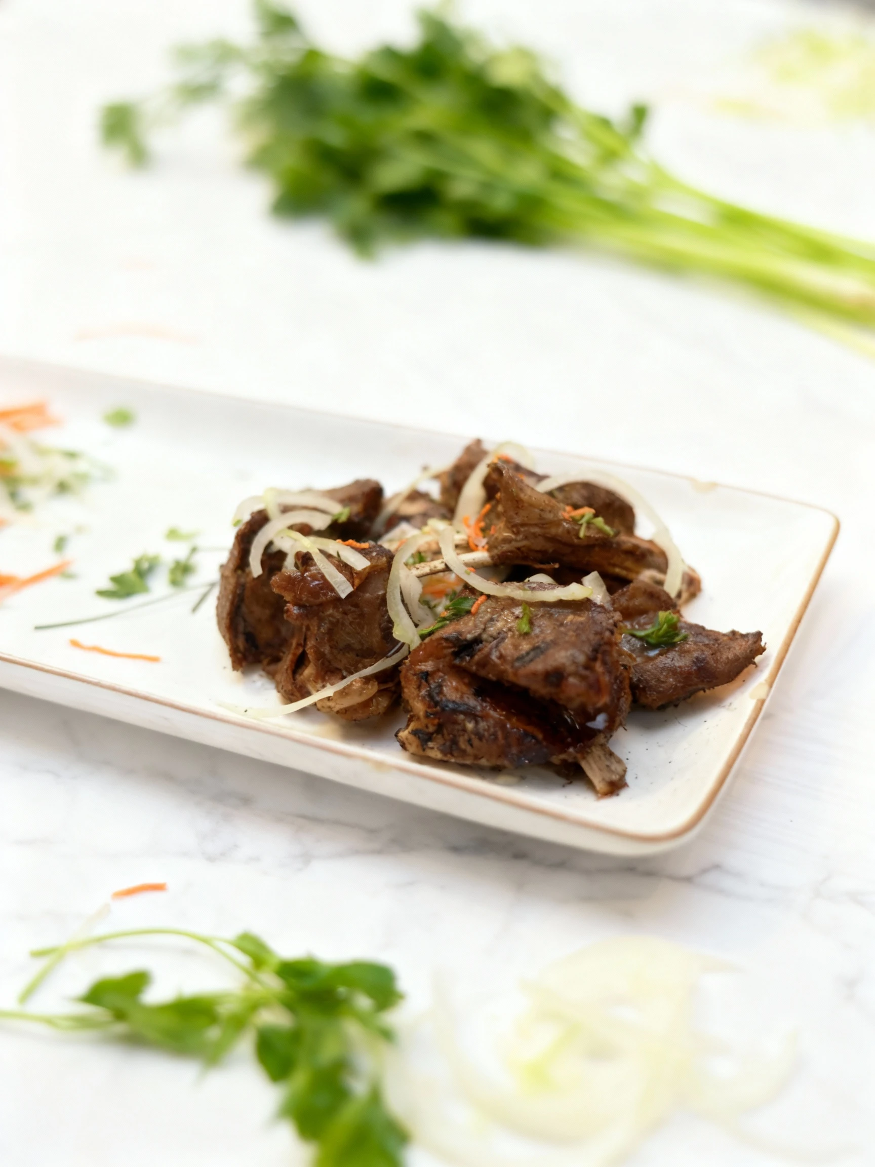 Pieces of grilled or roasted bone-in meat, likely ribs, are piled high and garnished with fresh slices of raw white onion, shredded carrots, and chopped green h