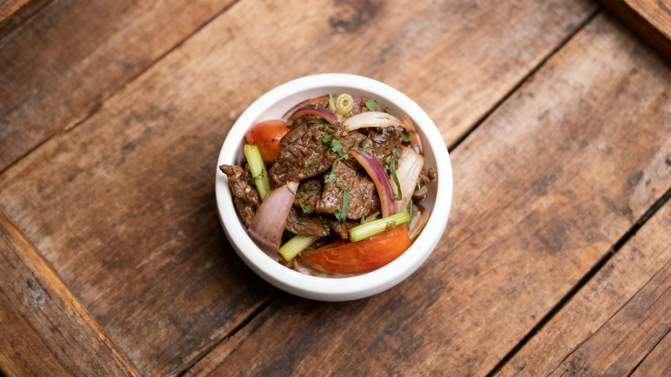Lomo saltado consisting of stir-fried beef strips, red onions, tomatoes, and green onions garnished with fresh herbs in a white bowl.