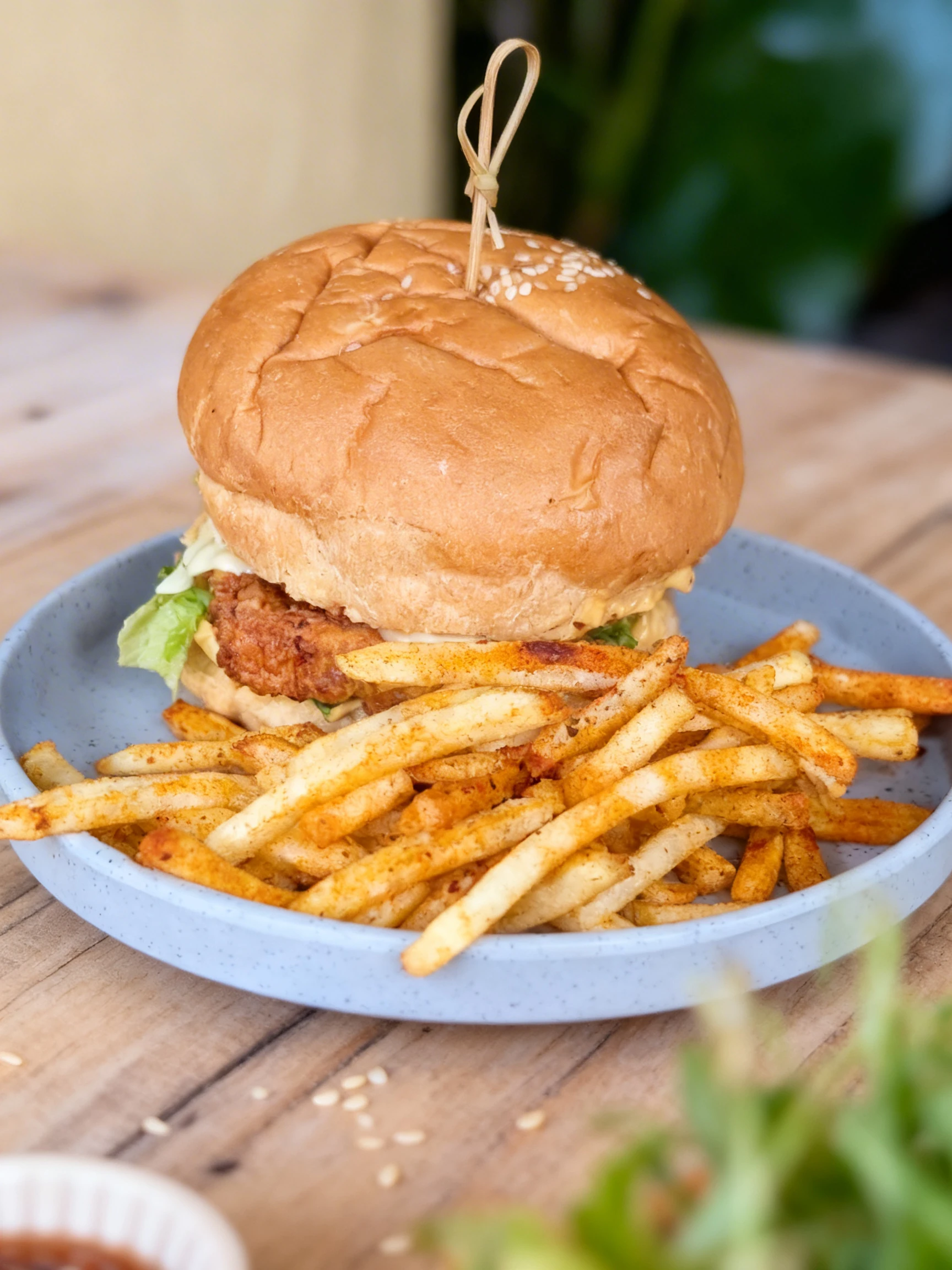 A fried chicken burger with lettuce and mayo on a sesame seed bun, served with a side of seasoned french fries.