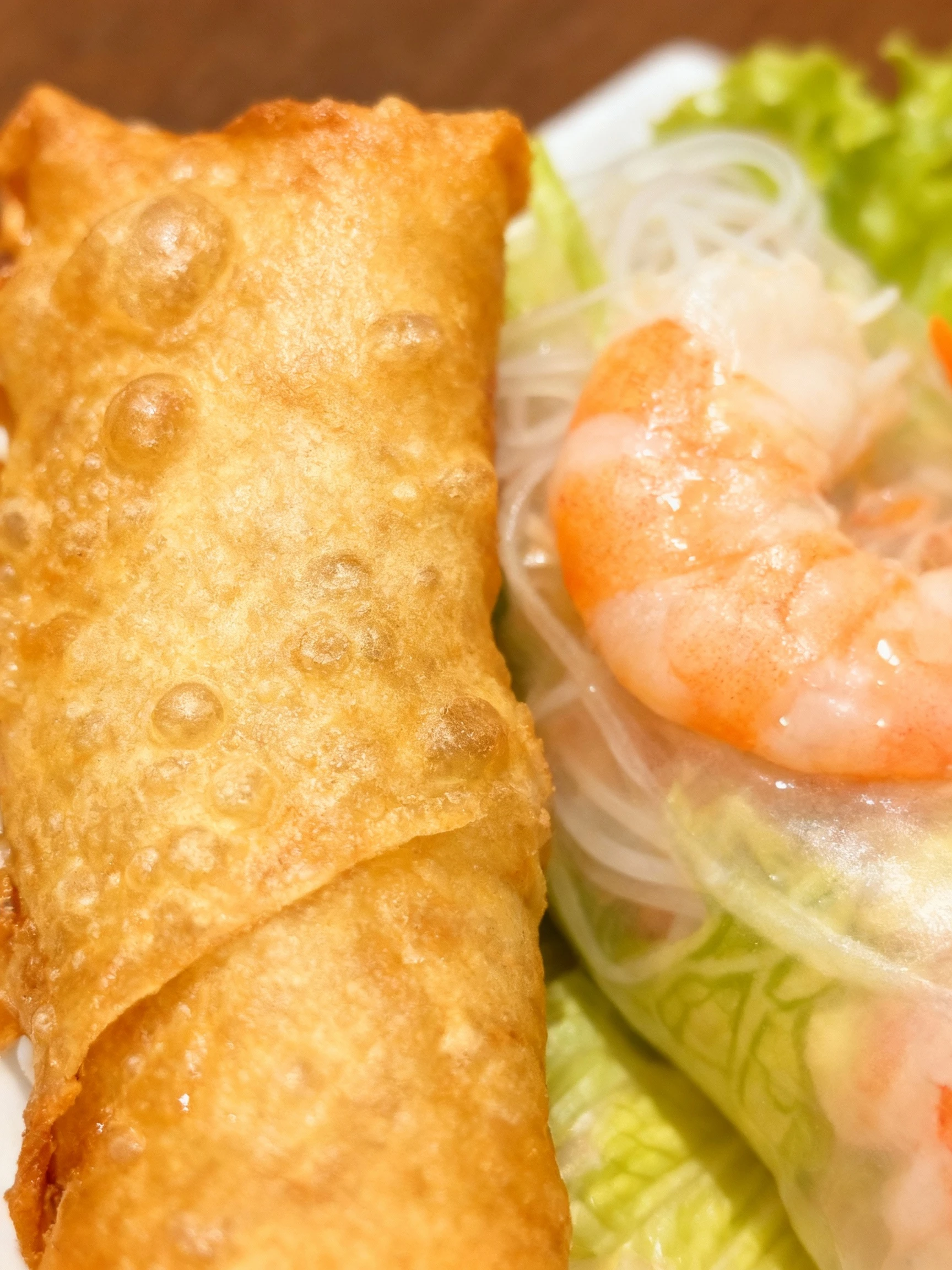 An appetizer spread featuring golden-fried spring rolls and fresh rice paper rolls filled with shrimp and vermicelli, served with contrasting peanut and sweet c