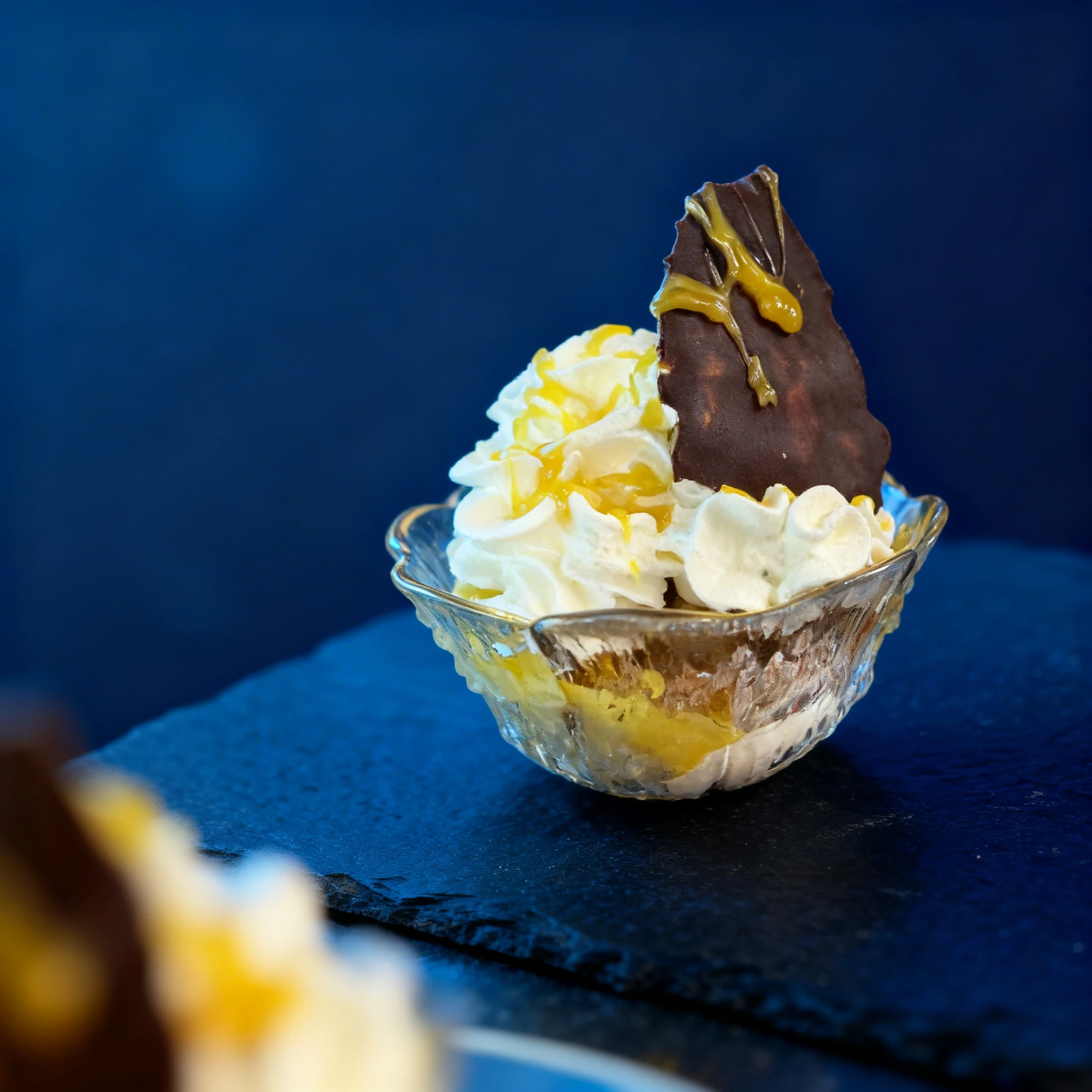 An ice cream sundae served in a glass bowl topped with whipped cream, yellow syrup drizzle, and a large chocolate shard.