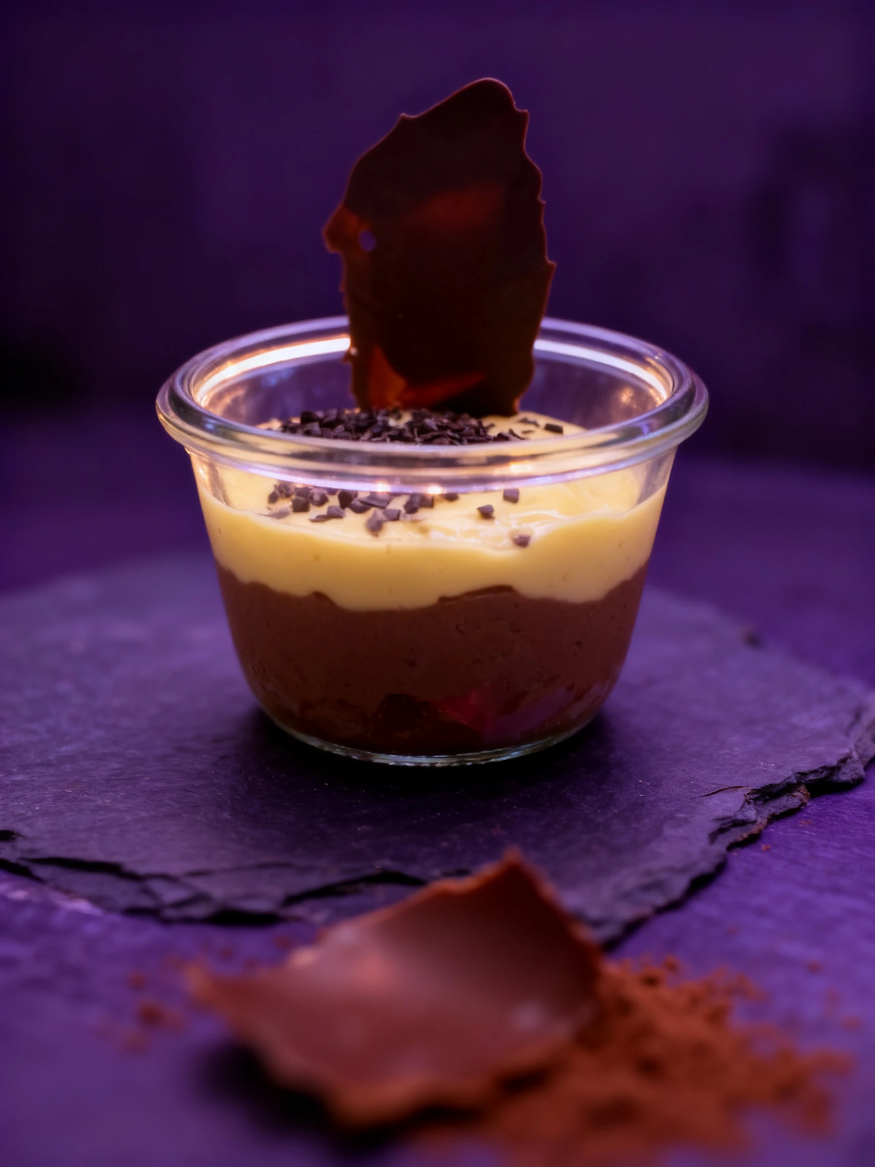 A layered chocolate and vanilla pudding topped with chocolate sprinkles and a large chocolate shard, served in a glass jar.