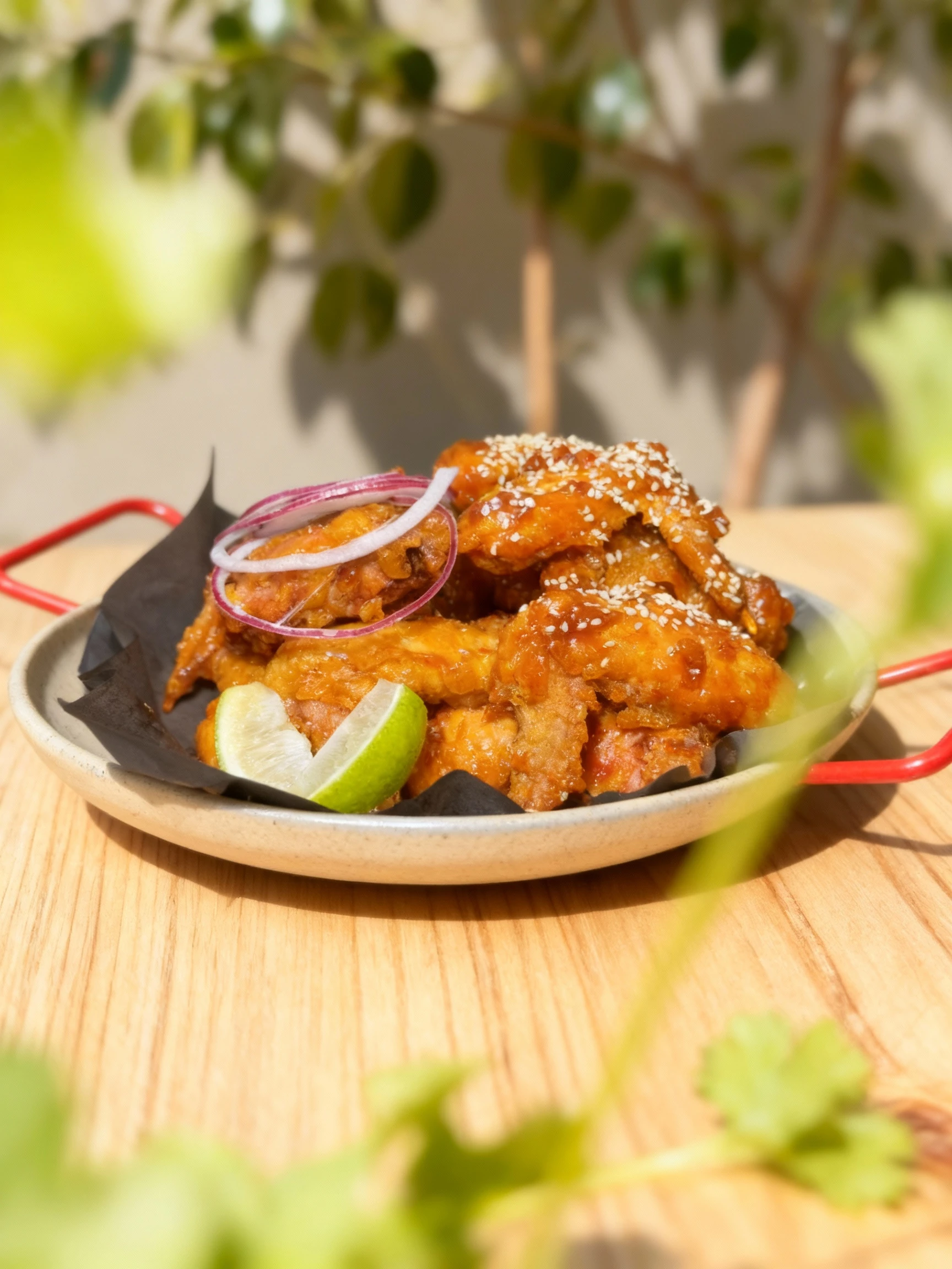 A large portion of glossy, fried chicken pieces coated in a sweet or spicy amber glaze and topped generously with white sesame seeds. The dish is garnished with