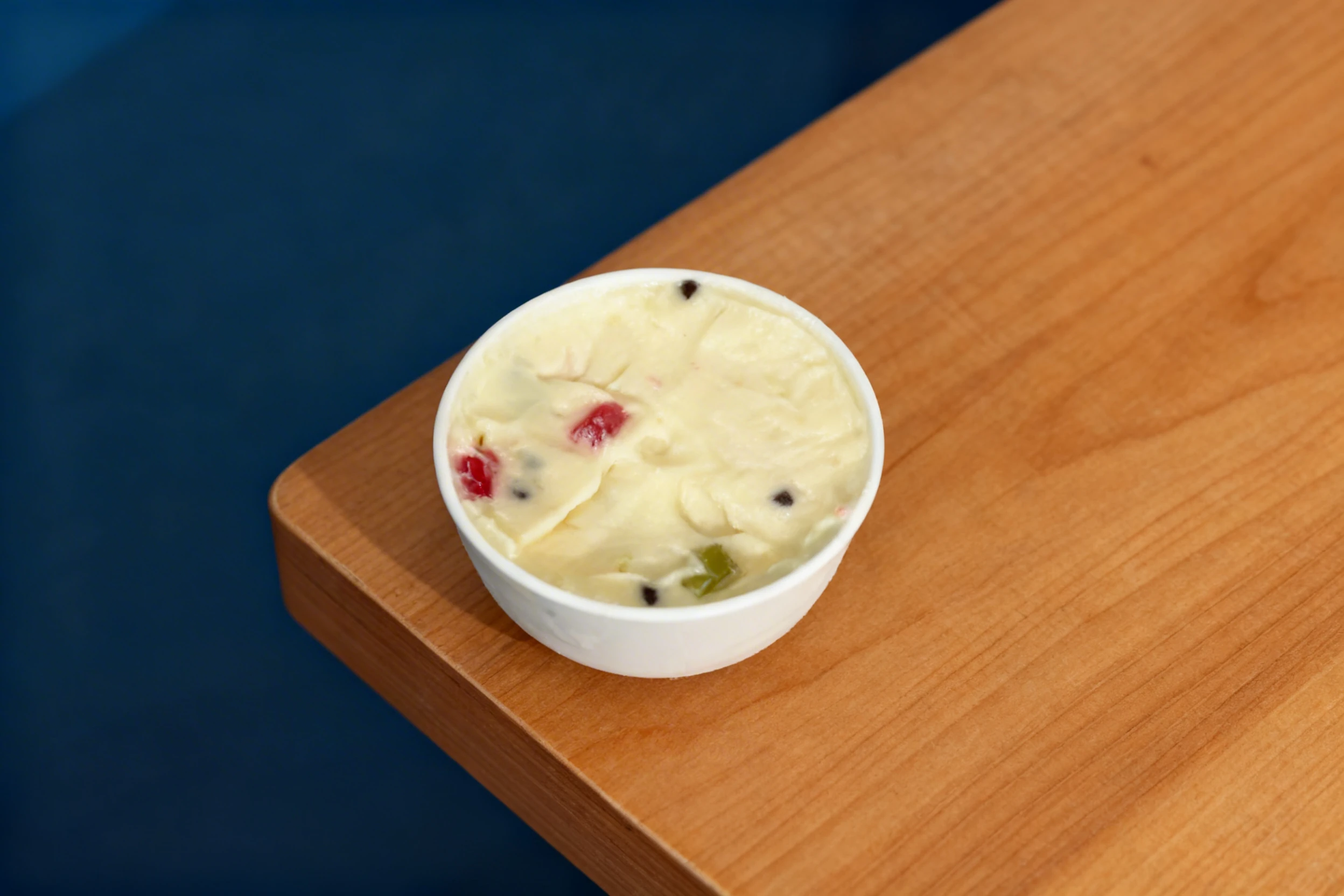 A single scoop of white ice cream or frozen yogurt containing dark chocolate chips and red and green gummy pieces.