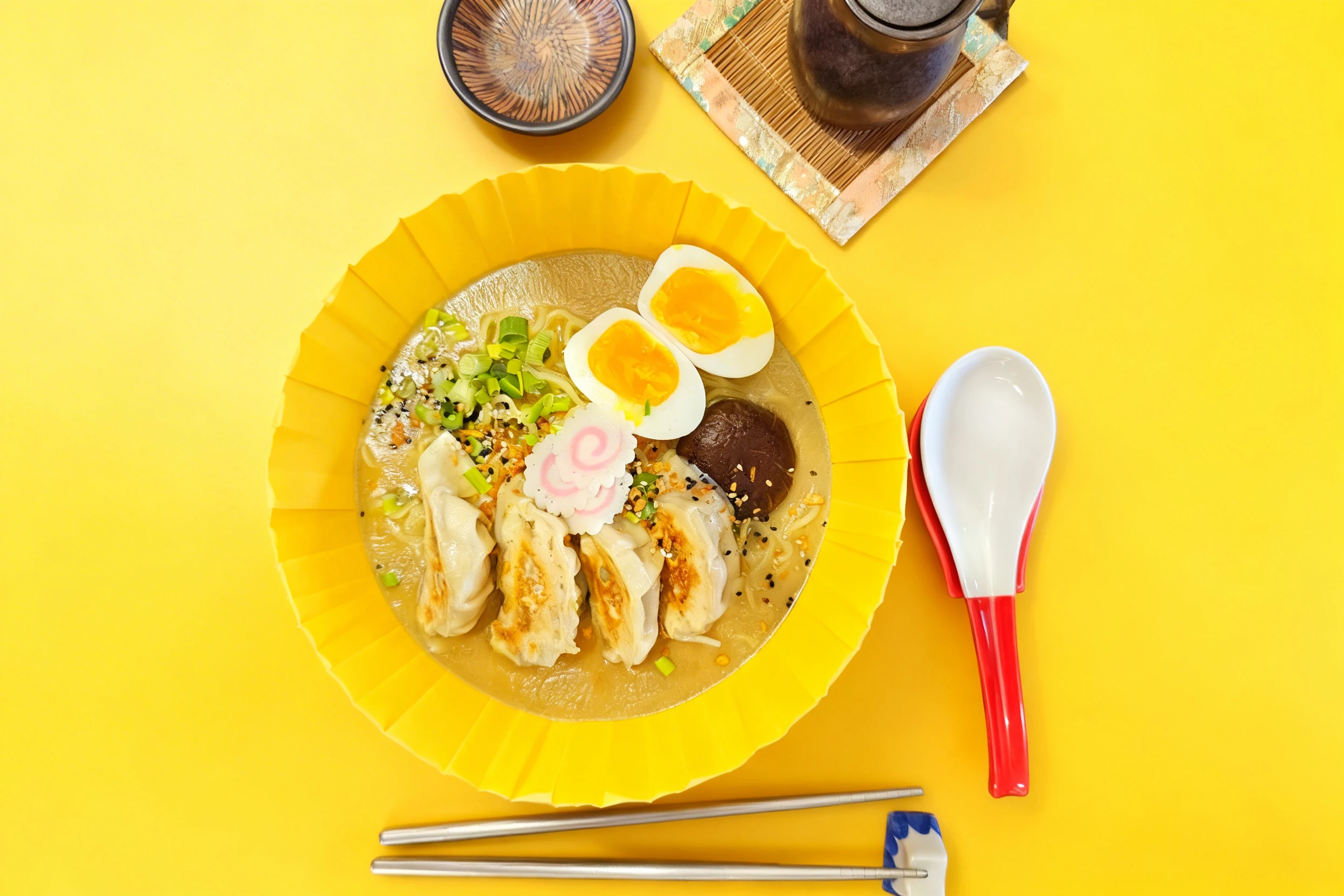 A bowl of ramen topped with four pan-fried gyoza, a soft-boiled jammy egg, narutomaki fish cakes, a shiitake mushroom, and sliced green onions in a savory broth