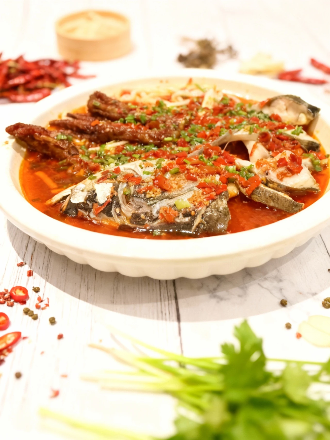 A spicy Chinese fish dish featuring segments of a whole fish and a head piece served in an oily, bright red chili broth, topped with chopped red peppers and chi