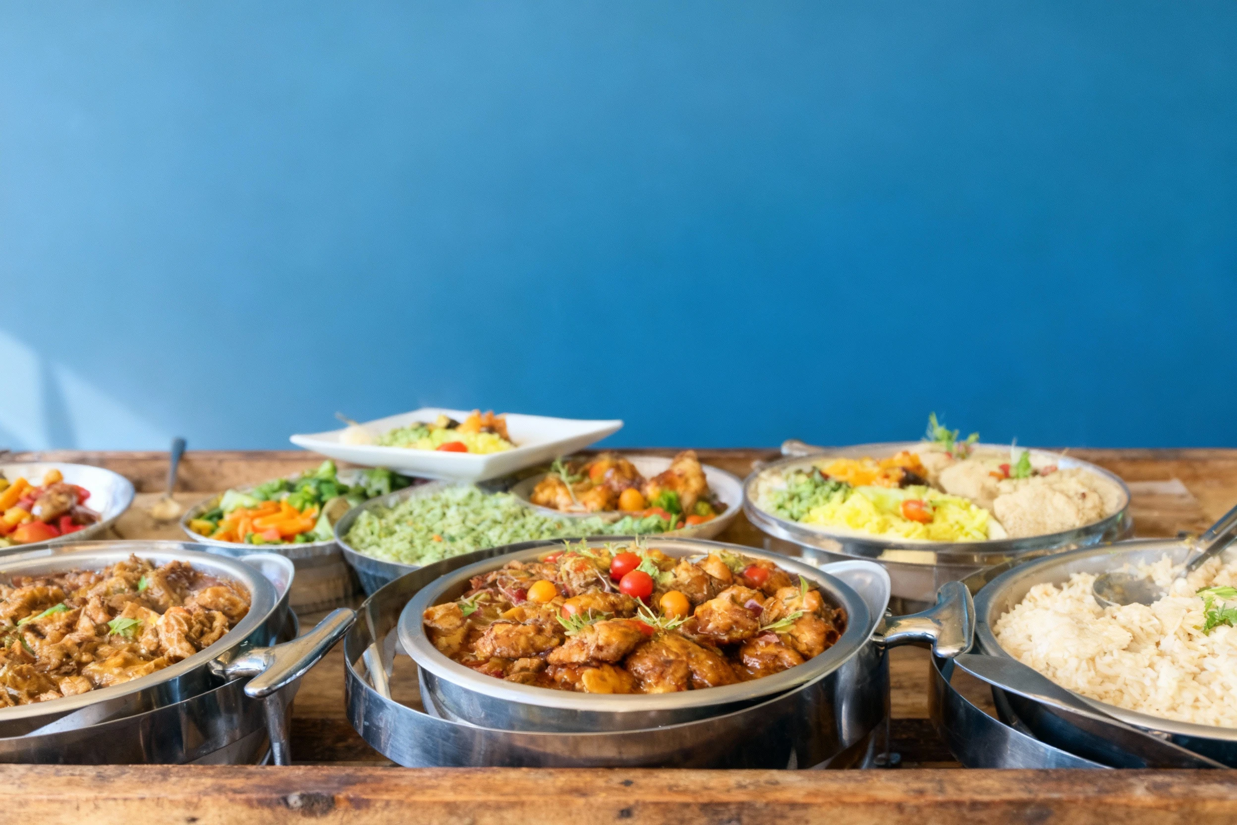 A view of a catering buffet setup featuring several chafing dishes filled with different prepared foods, including a rich meat stew, glazed chicken pieces garni