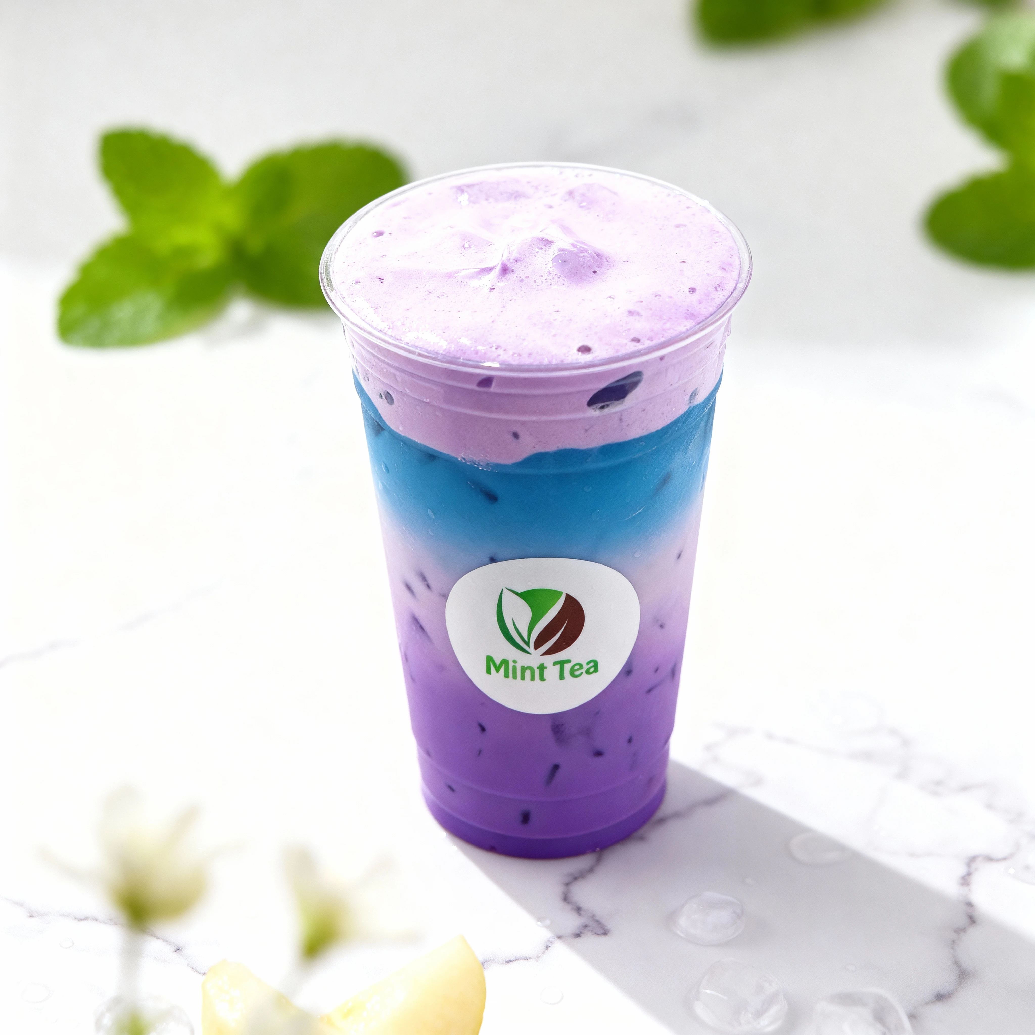 Layered iced beverage featuring a gradient of deep purple and bright blue liquid, topped with a thick, smooth layer of light purple foam or cream, served in a c