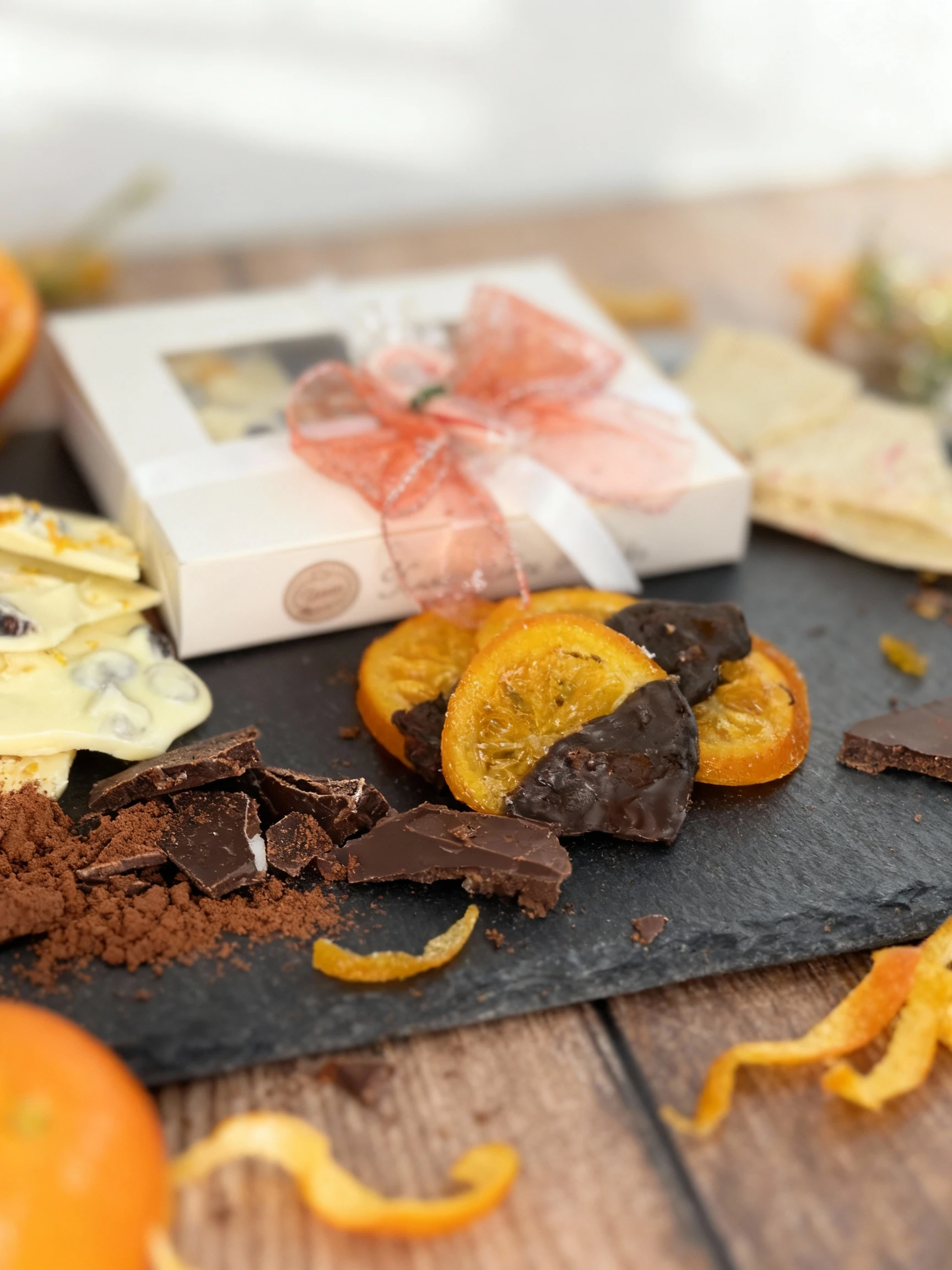A holiday assortment featuring a white gift box filled with various chocolates or candies, surrounded by pieces of white chocolate bark and candied orange slice