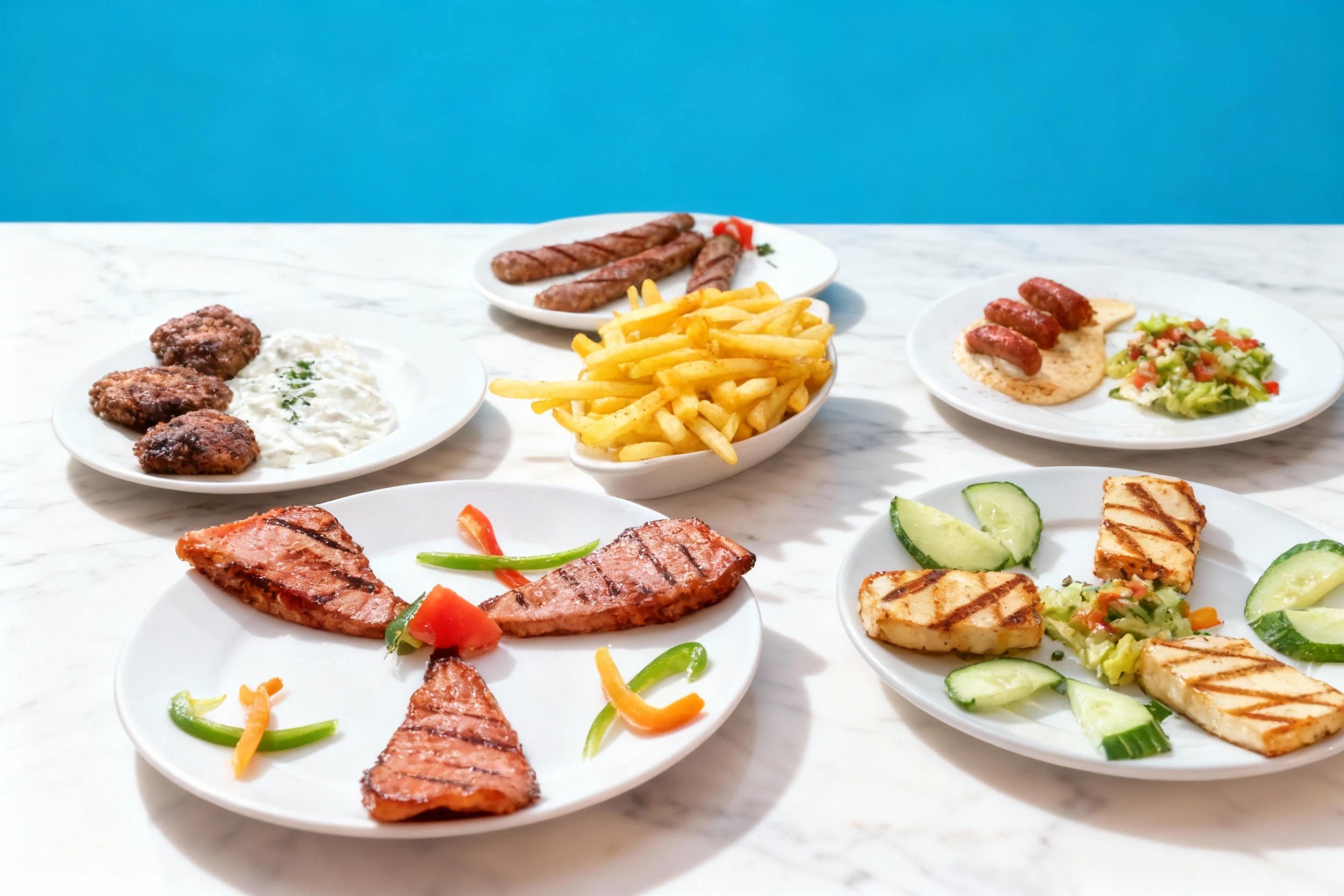 An overhead spread of various grilled dishes, including plates of grilled sausage and kofte served with tzatziki, grilled halloumi cheese with cucumber and dice
