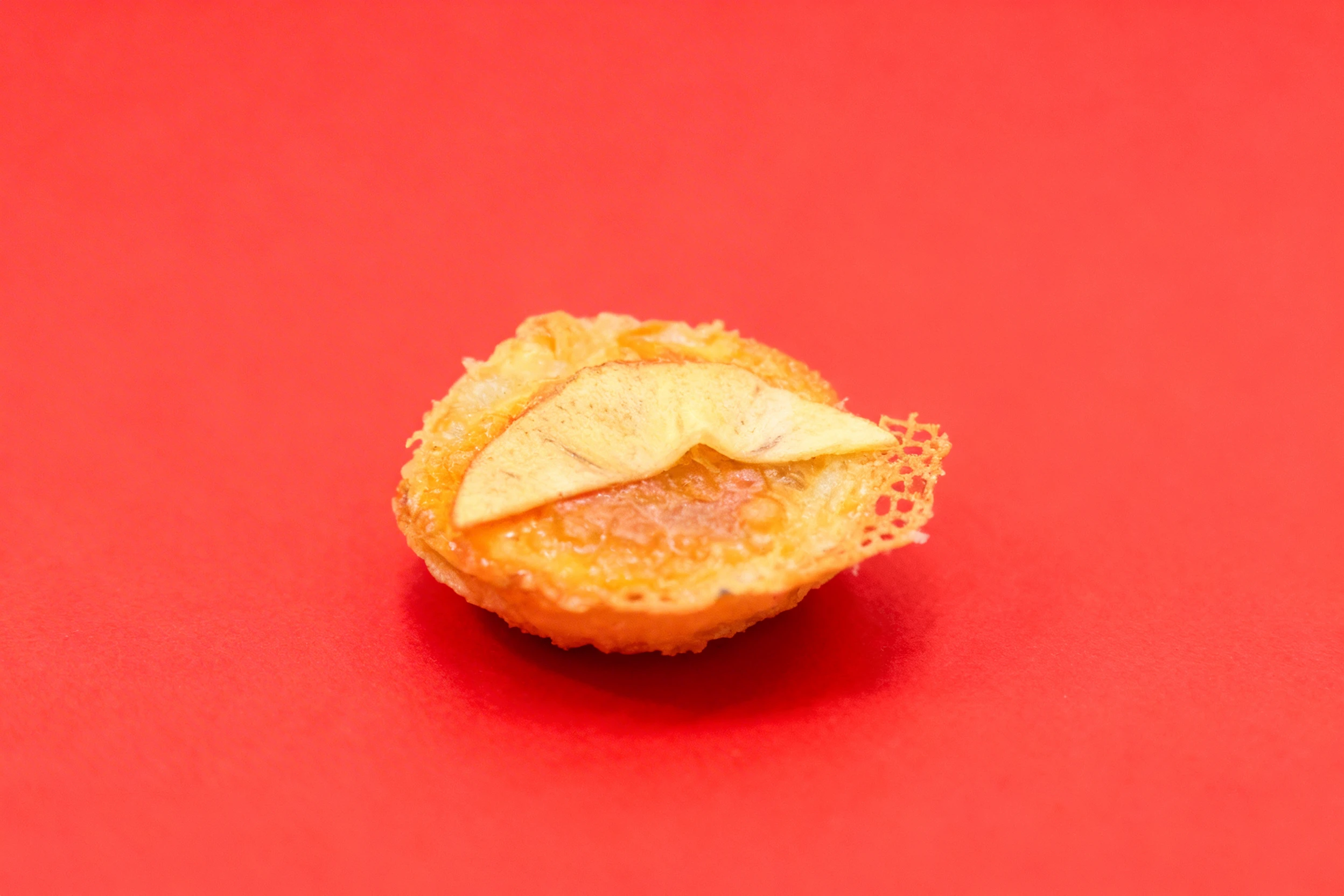 A small round pastry or cheese crisp topped with a thin fruit slice, served in a black bowl with a thin layer of sauce or oil.
